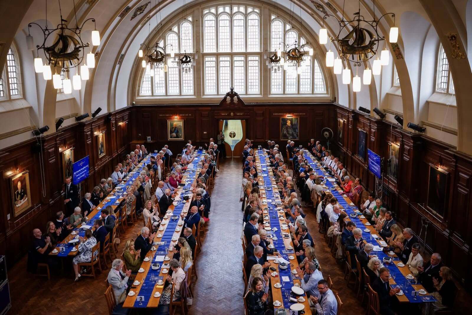 Guests applauding at long tables in the hall at Britannia Royal Naval College, Dartmouth