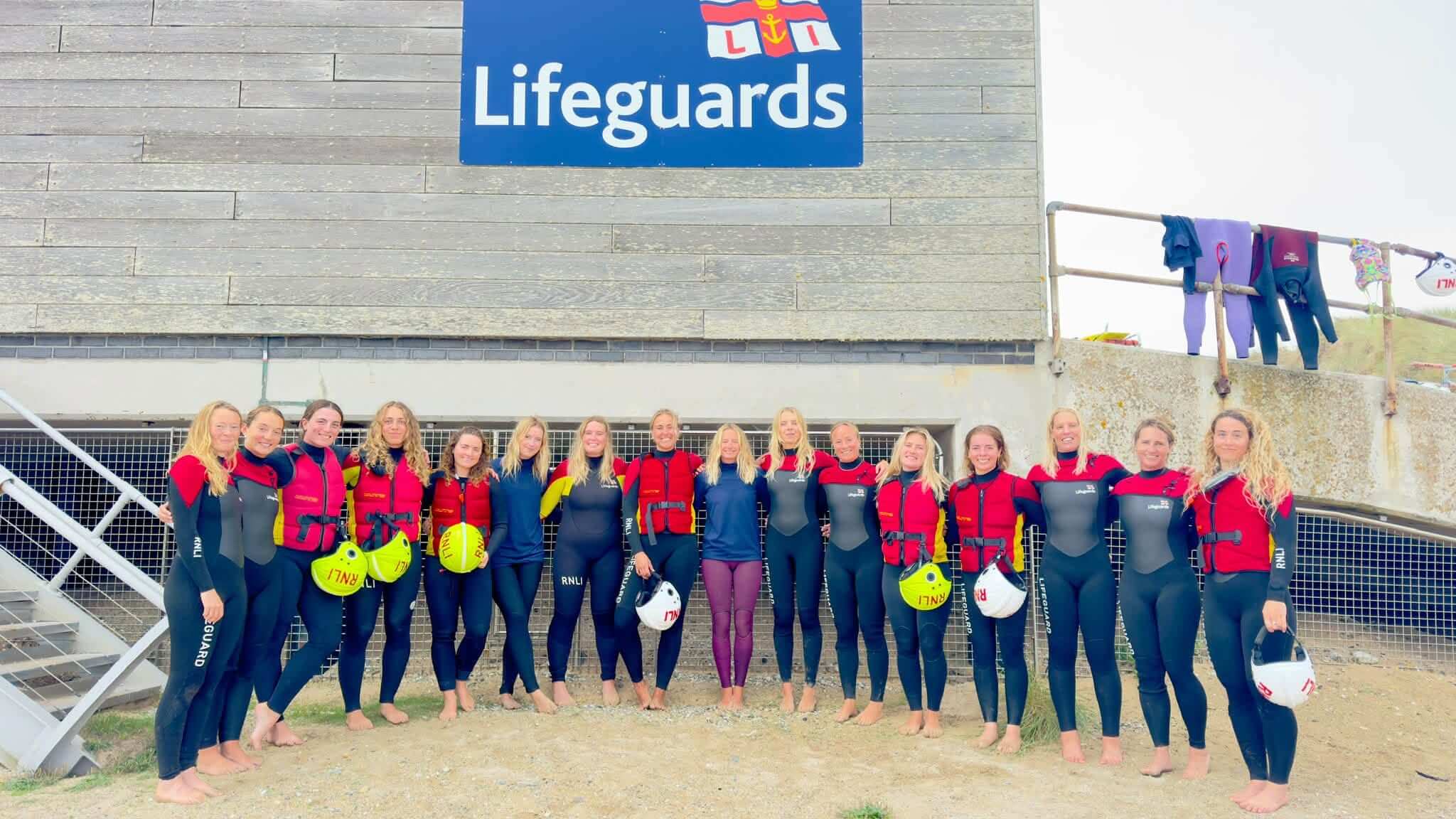 A group of women lifeguards lined up beneath an RNLI Lifeguards sign
