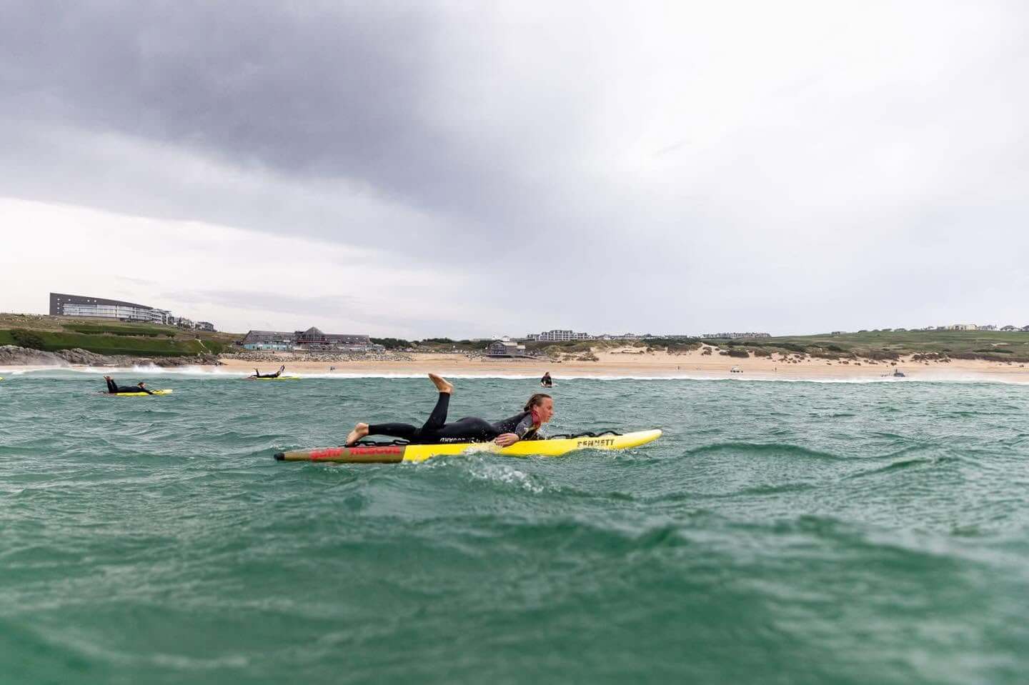 A lifeguard paddling a yellow rescue board in green water off a sandy beach