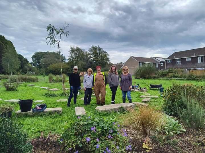 Five volunteers standing in Tredanek Meadow in Bodmin, with planted beds in the foreground