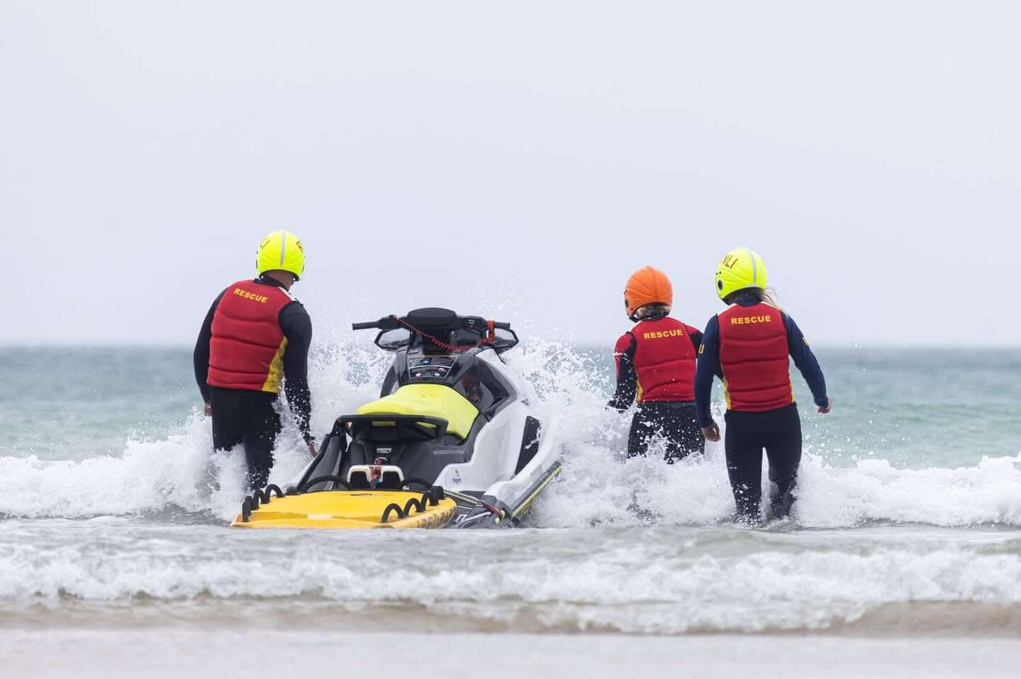 Three crew in rescue vests and helmets launching a rescue water craft into the surf