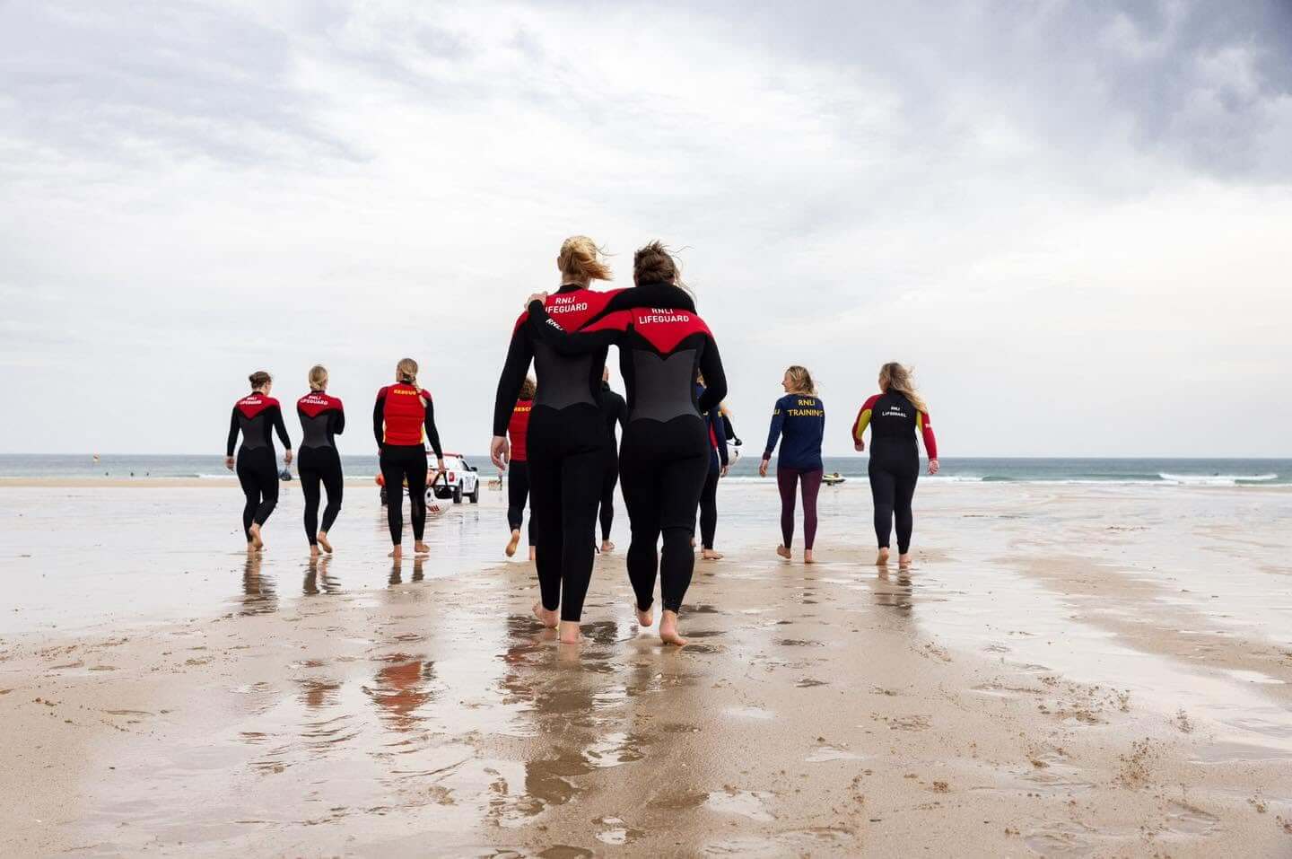 RNLI lifeguards in wetsuits walking down a wet beach towards the sea