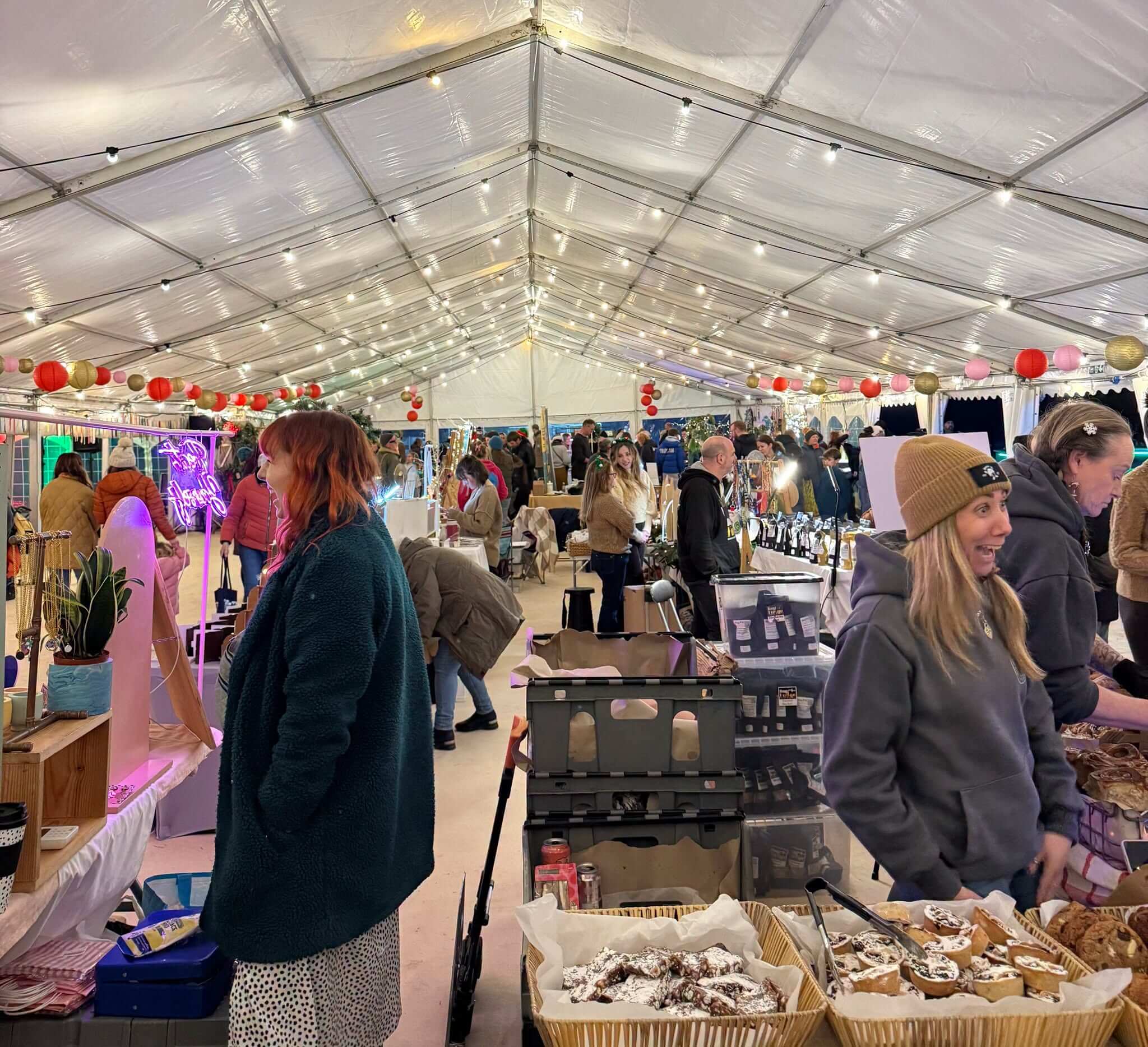 Stalls and shoppers inside a marquee market with festoon lights