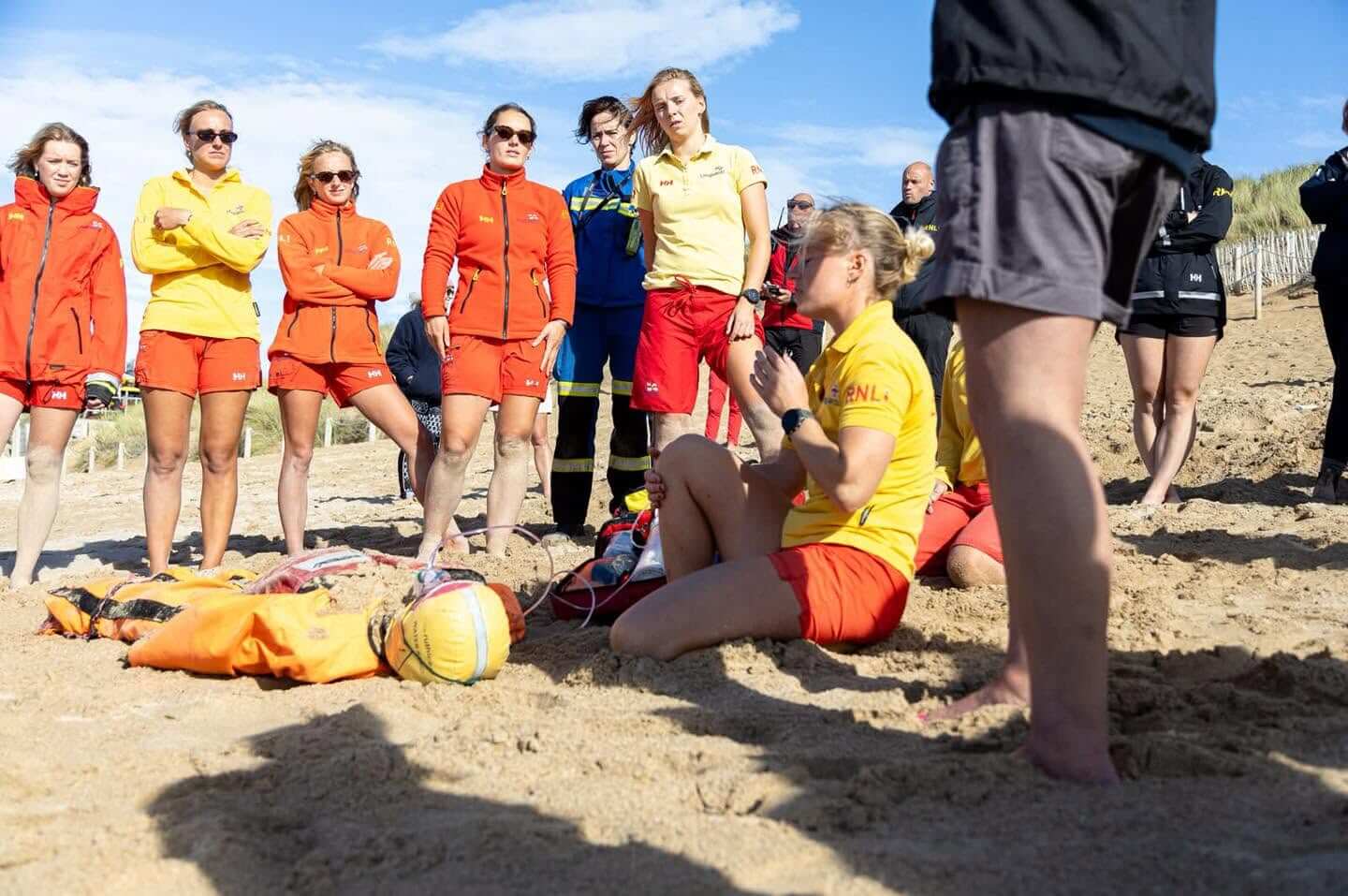 Lifeguards in red and yellow RNLI kit gathered on the sand around rescue equipment