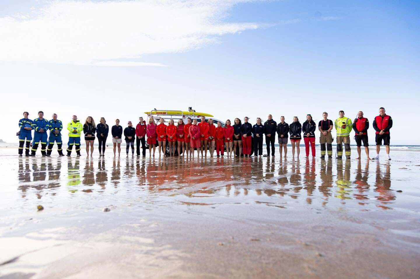 A long line of lifeguards and emergency service crews standing on a beach in front of a rescue vehicle