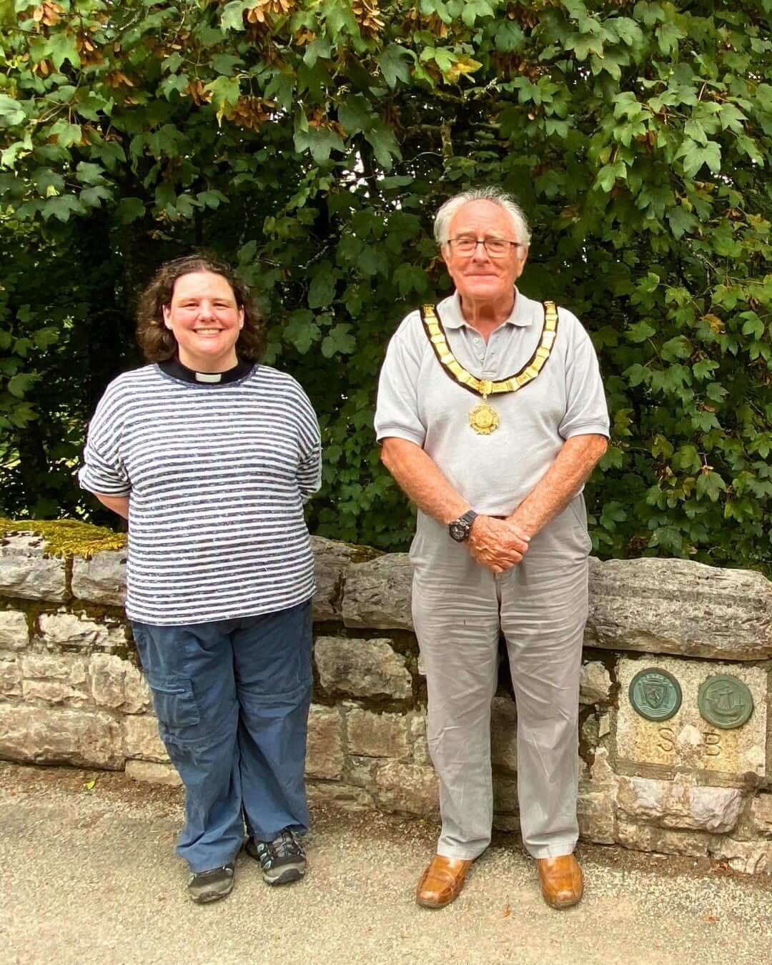 Two people standing beside a boundary stone set in a wall