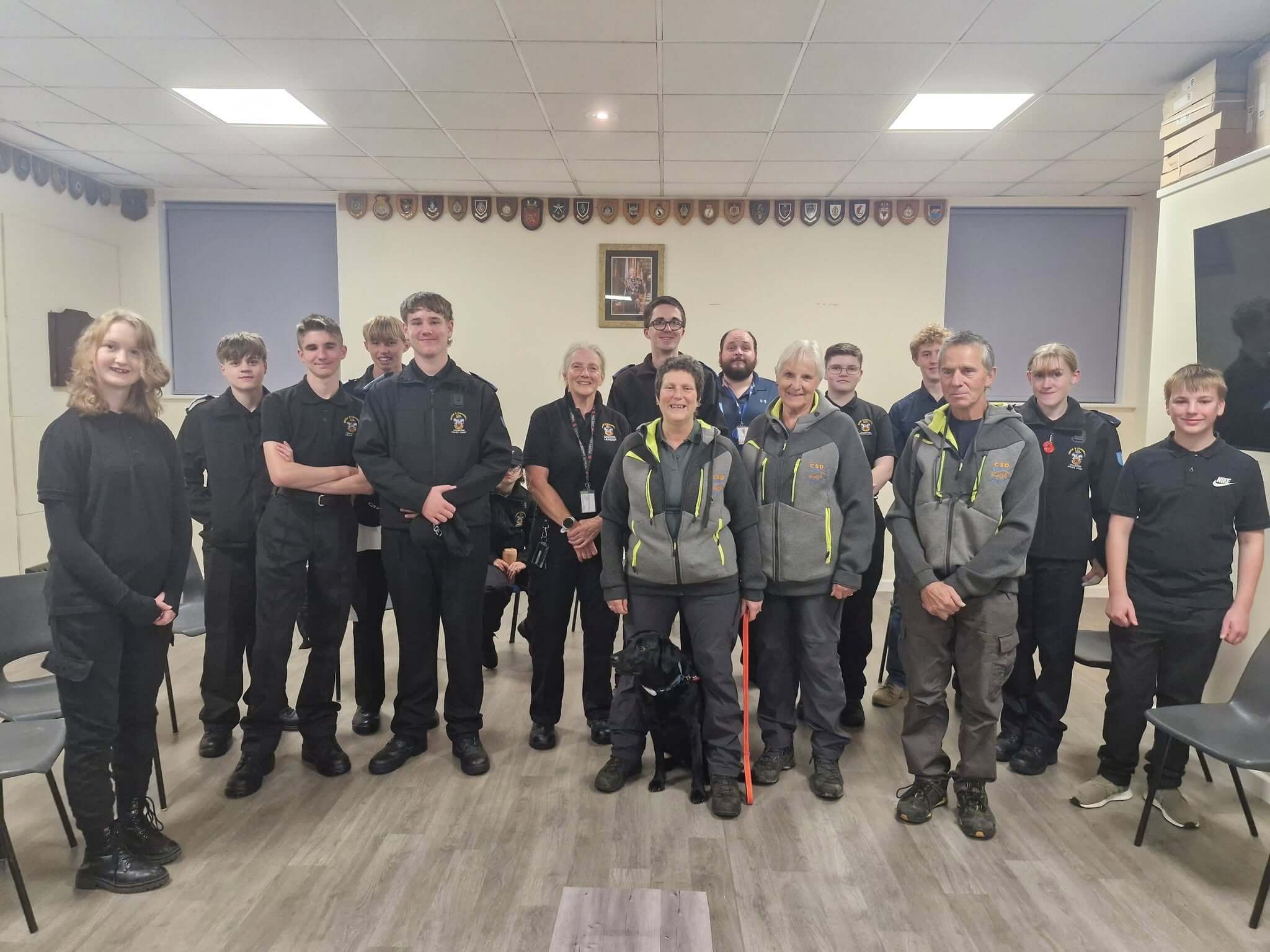 Launceston Police Cadets and Cornwall Search Dogs volunteers standing in a hall with a black search dog