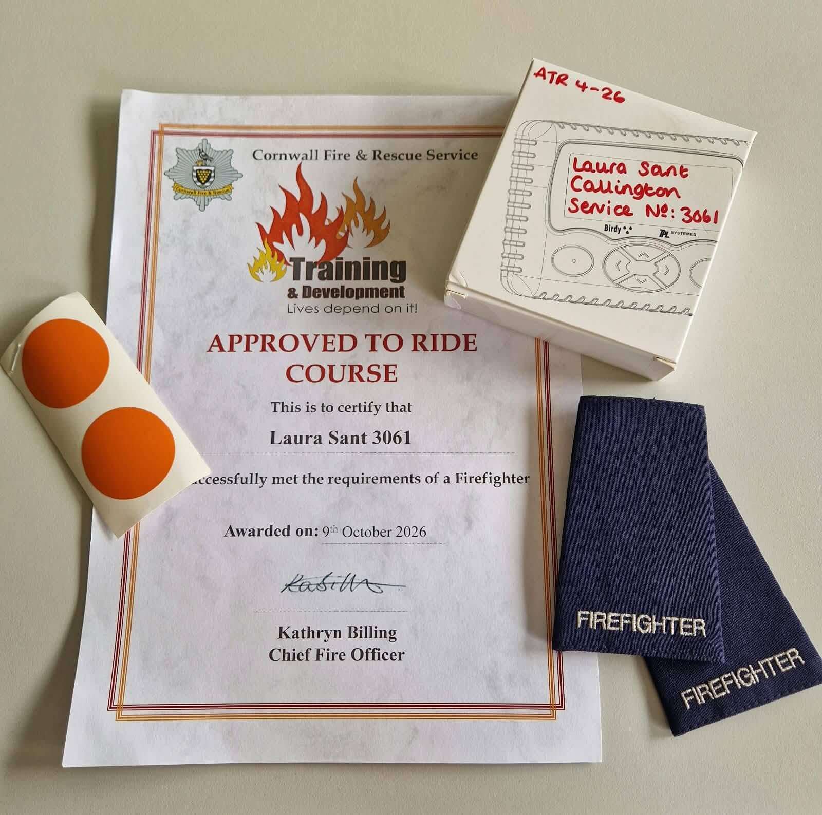 Laura Sant's Approved to Ride certificate with firefighter epaulettes and a pager box