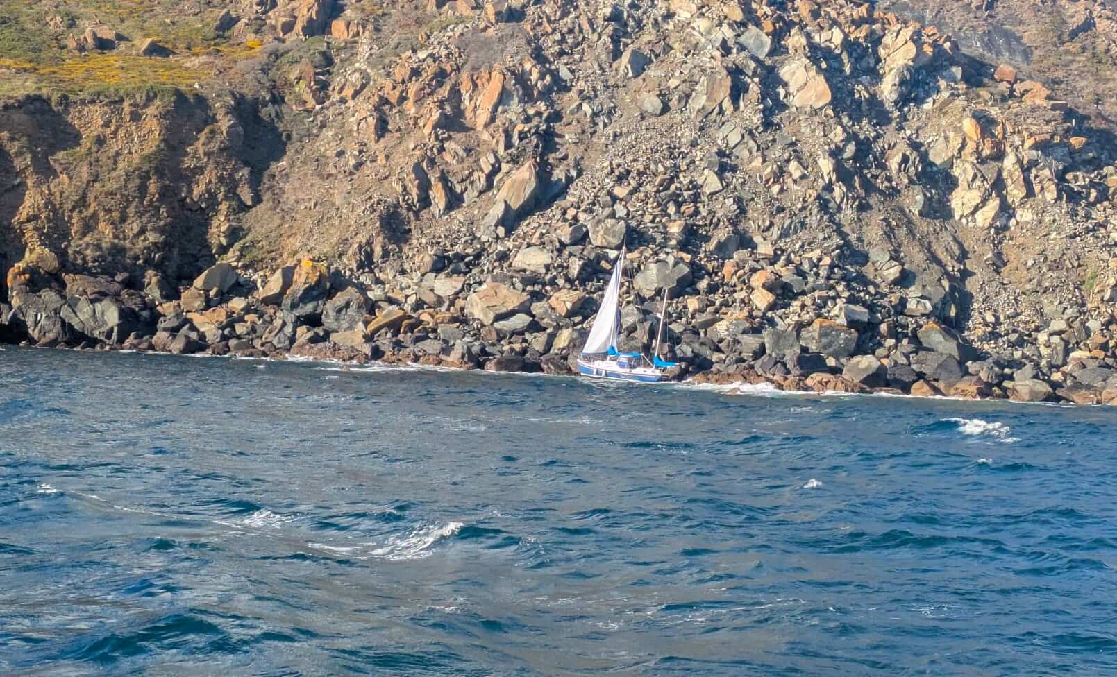 Damaged yacht pinned against rocks below cliffs near Black Head on The Lizard