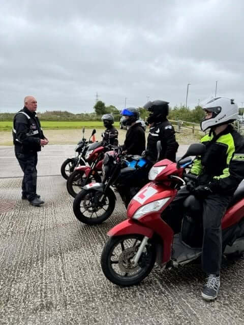 Young riders on mopeds and motorcycles listening to a Gear Up instructor