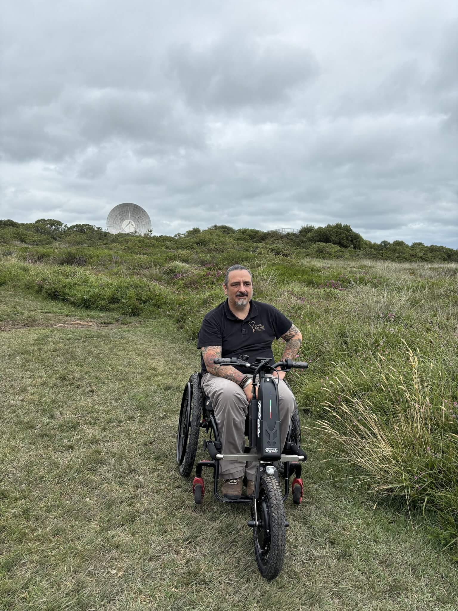 A man using an off-road wheelchair attachment on grass with a satellite dish behind