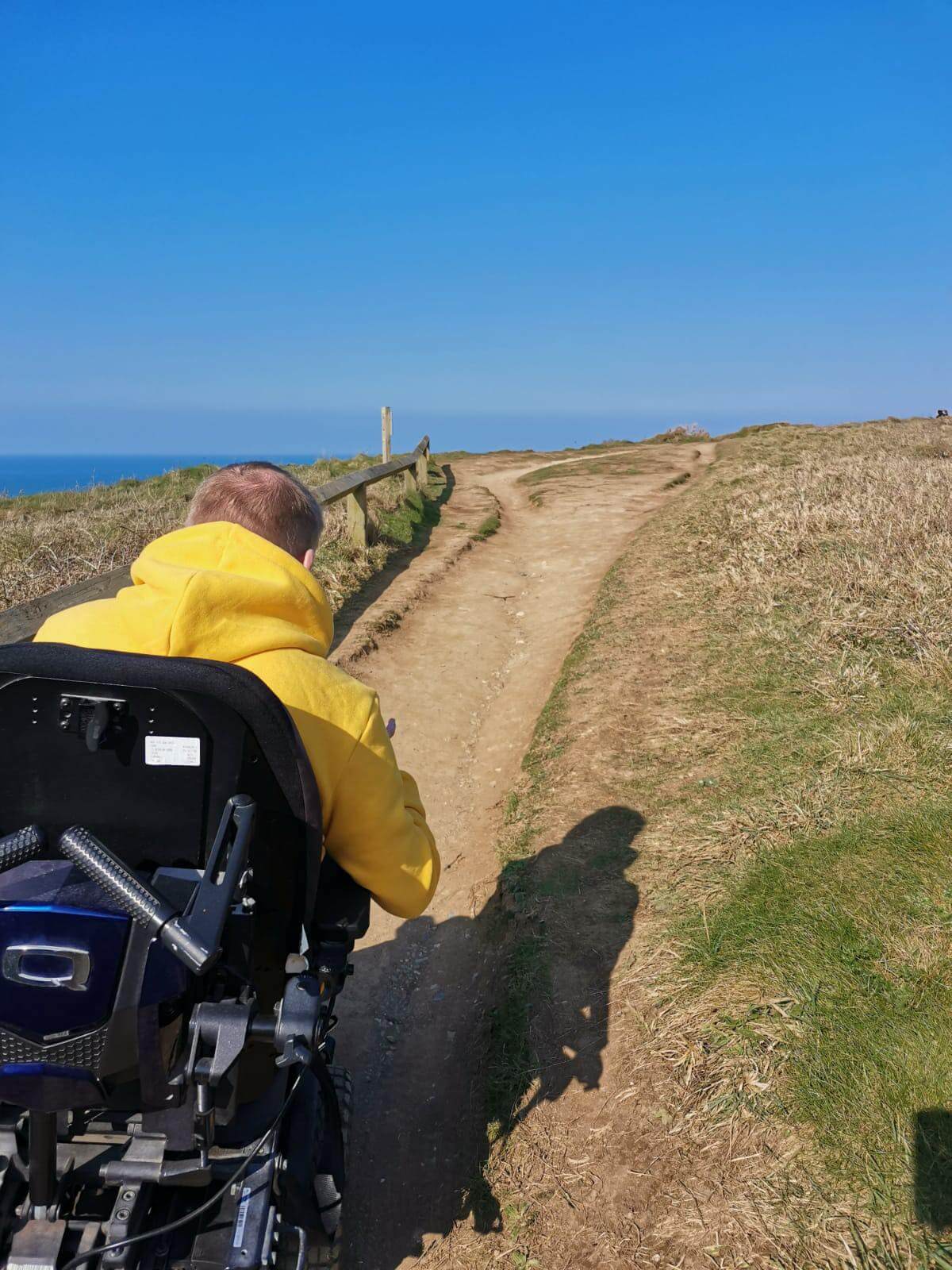A powerchair user on a coastal path under blue sky