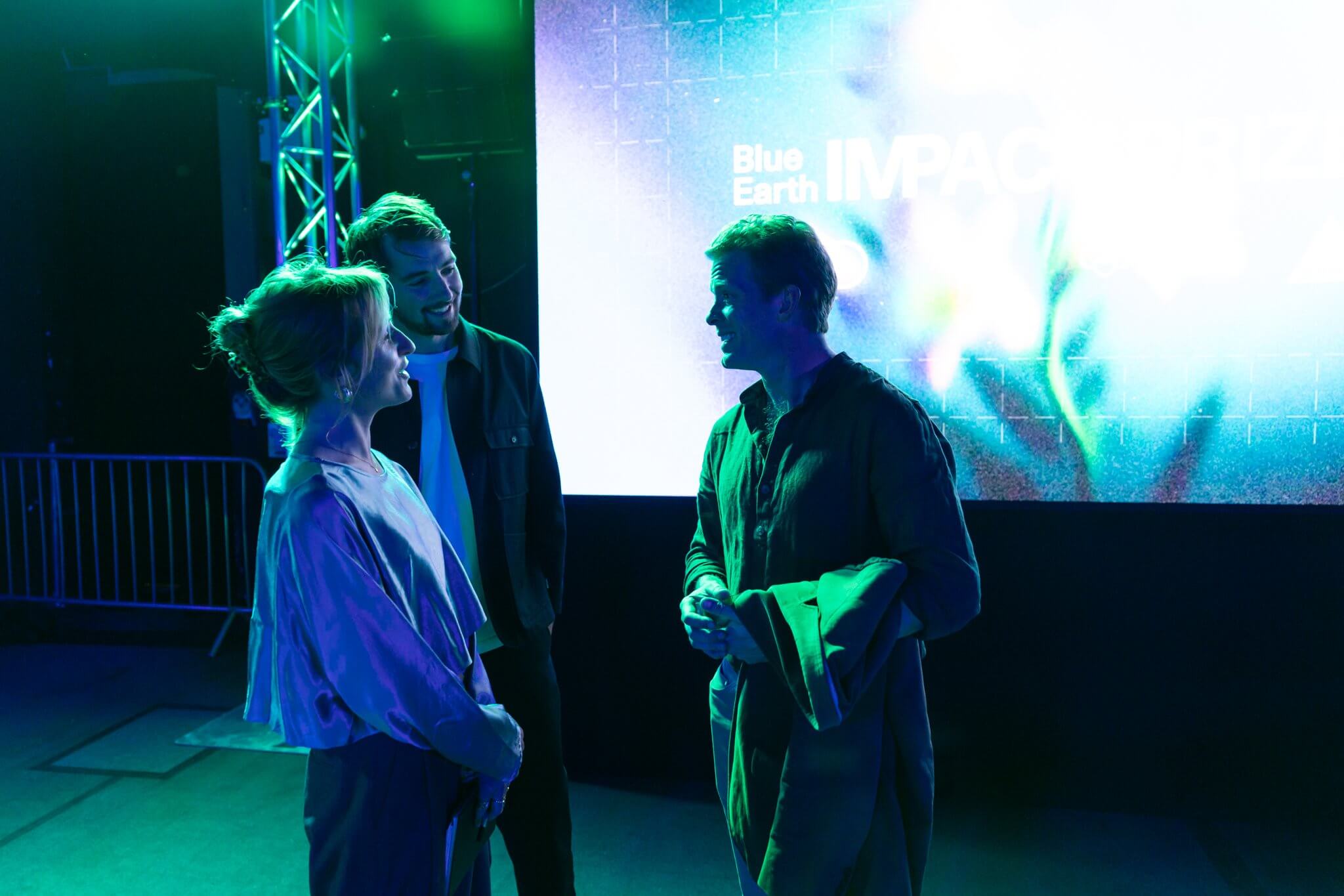 Three people talking in front of the Blue Earth IMPACT Prize screen at Blue Earth Summit