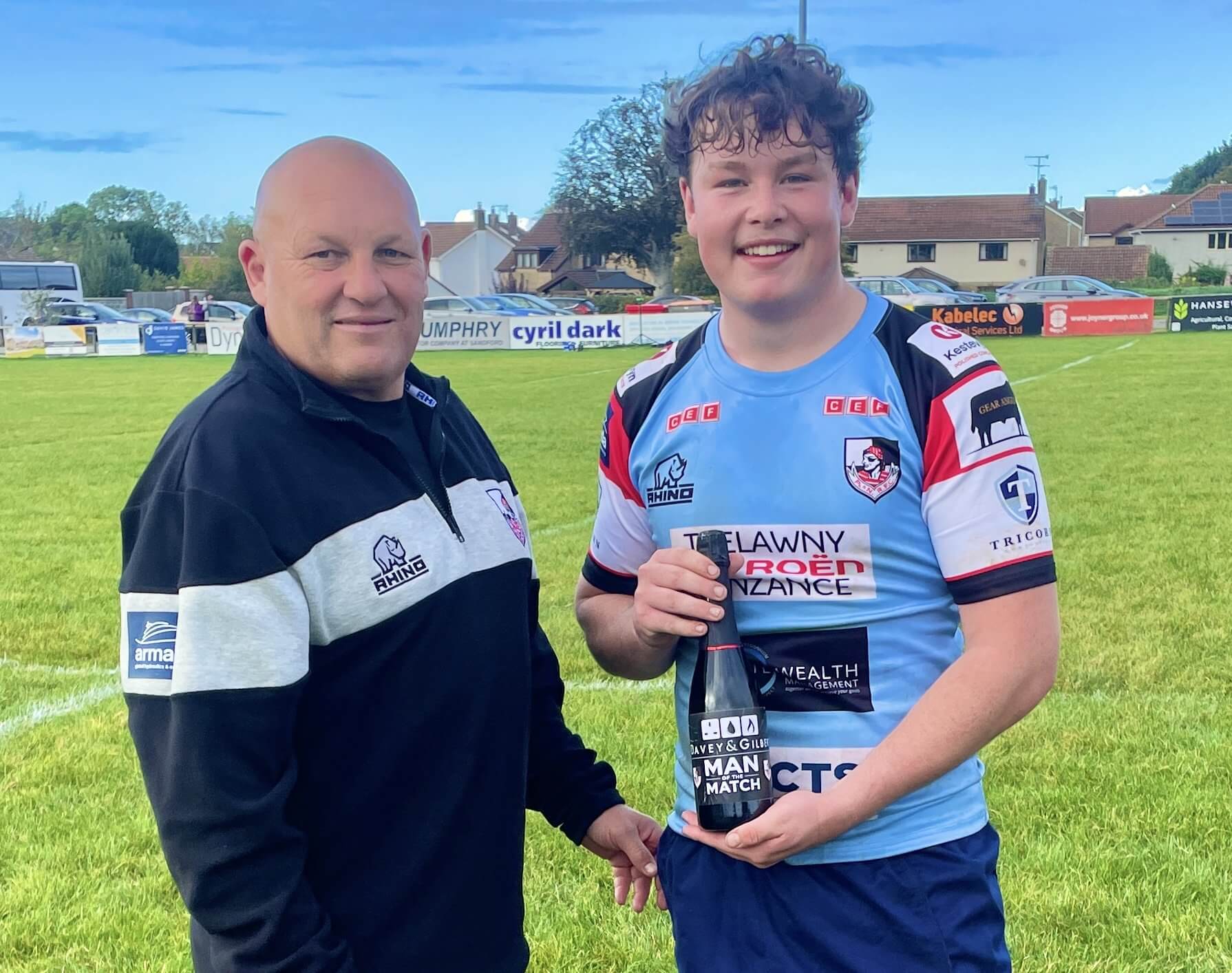 Callum Walsh holding a man of the match bottle beside Andrew Snell on the pitch at Winscombe