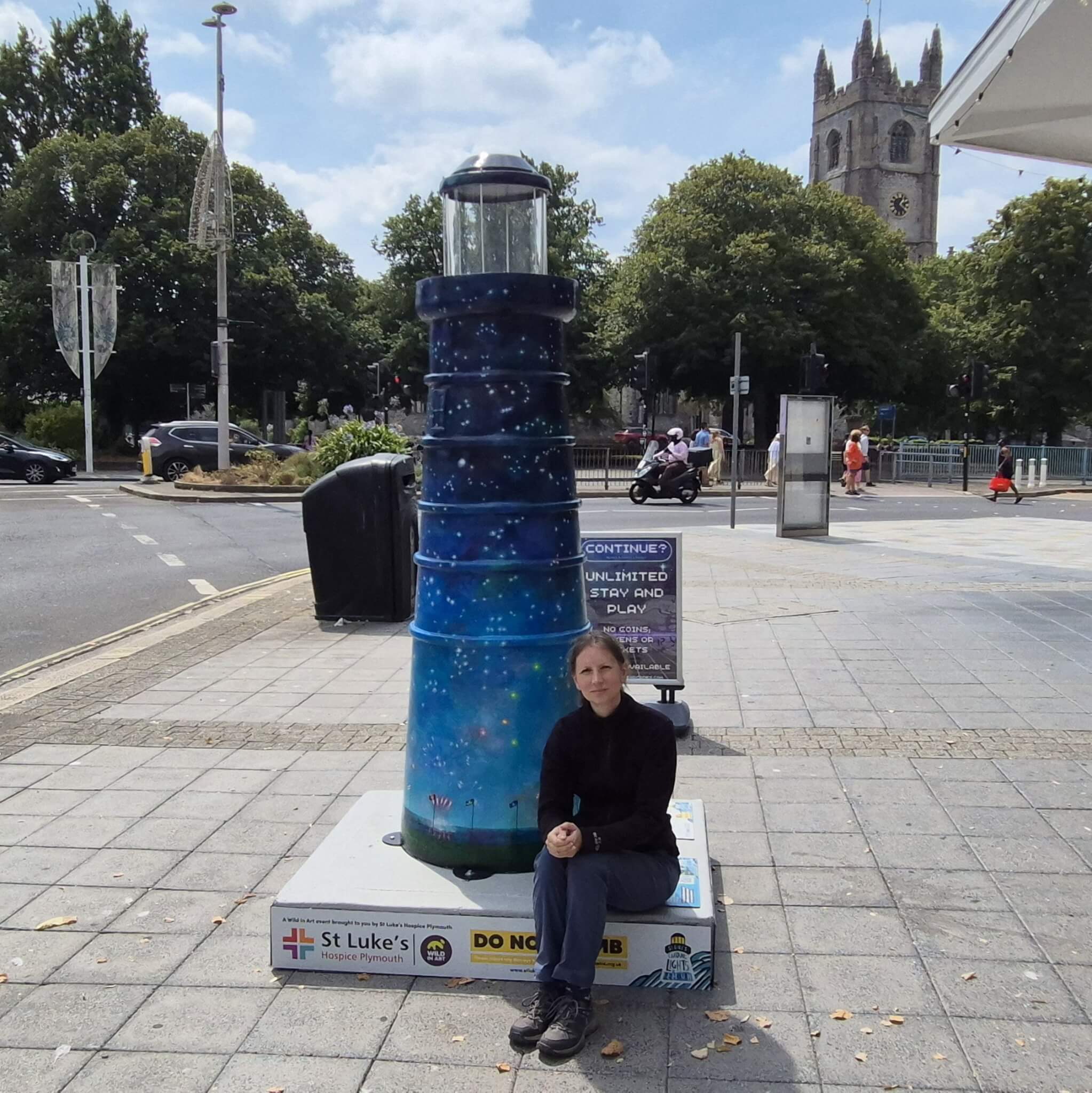 Artist Diane Griffiths sitting beside her Celestial Beacon lighthouse sculpture in Plymouth