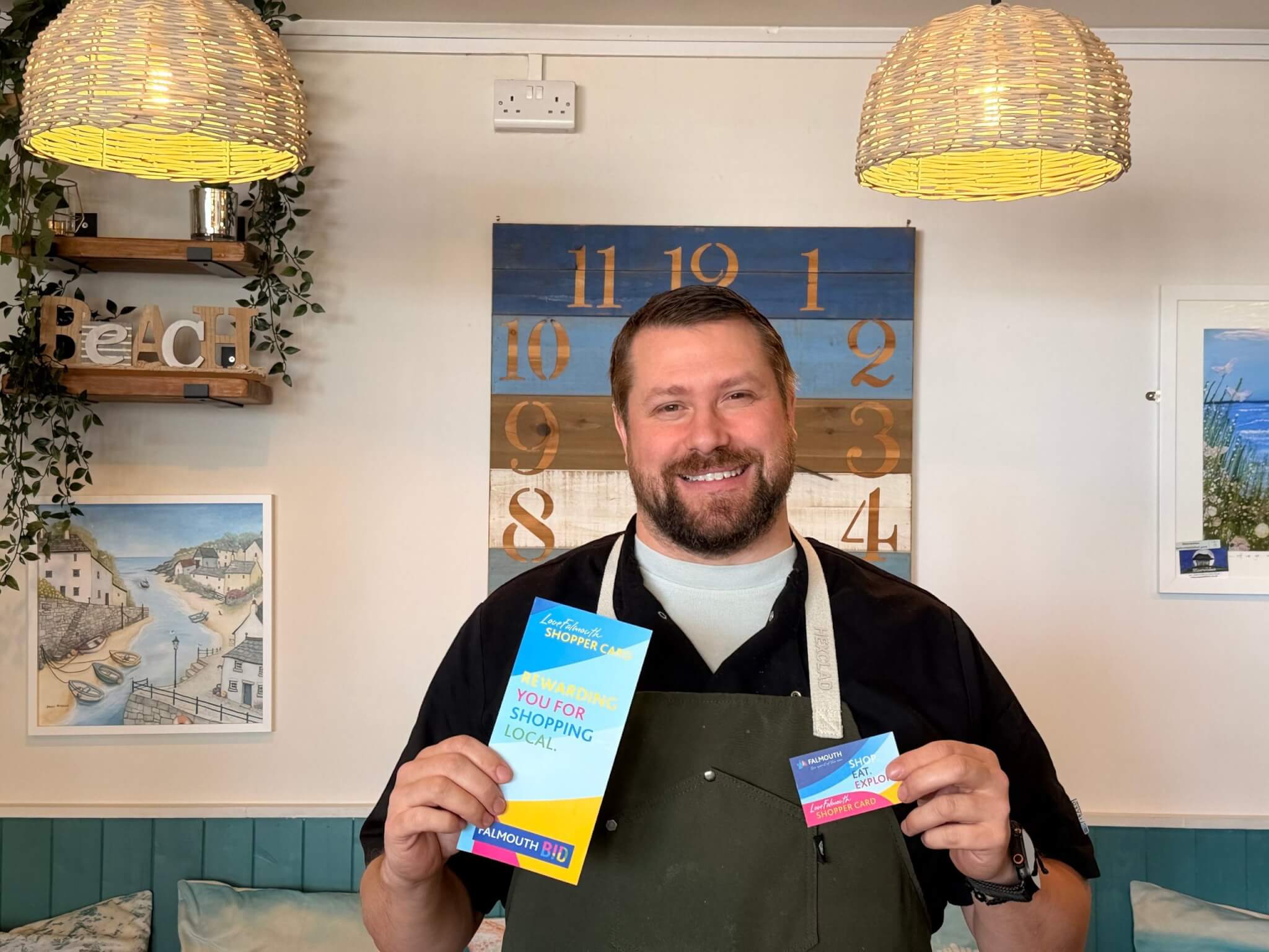 Chris at Koffiji in Falmouth holding a LoveFalmouth Shopper Card and leaflet