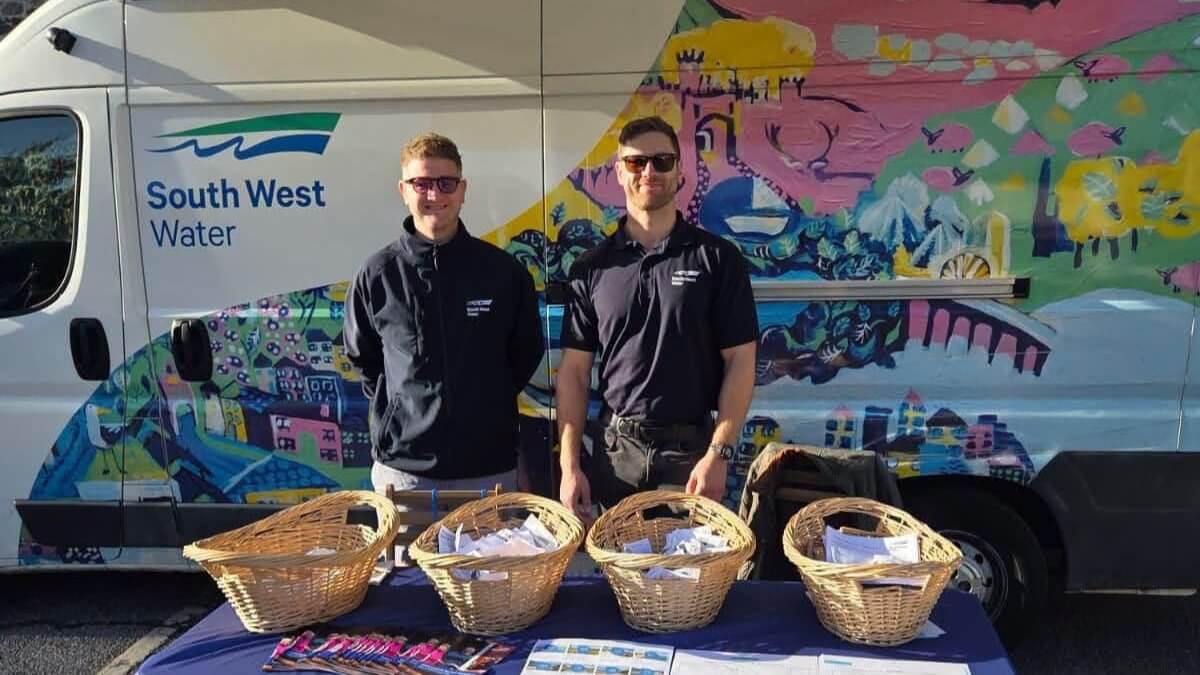 Two South West Water staff at a community drop-in stand in front of a painted van