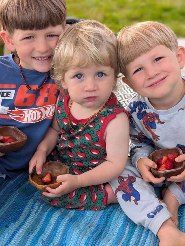 Em's three young sons sitting on a blue rug holding bowls of strawberries