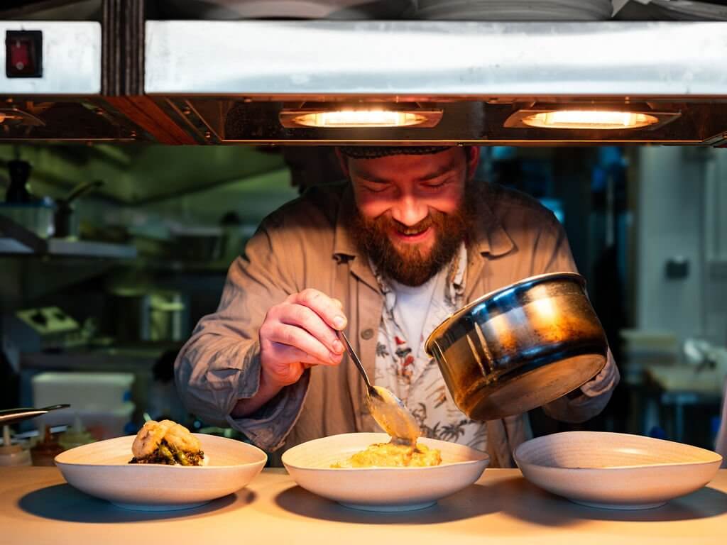 Chef plating dishes under the heat lamps at the pass