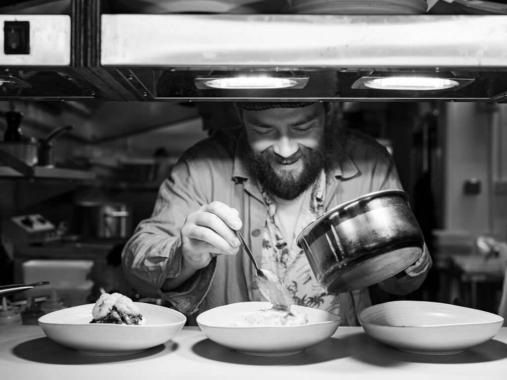 Black and white shot of a chef plating dishes at the pass