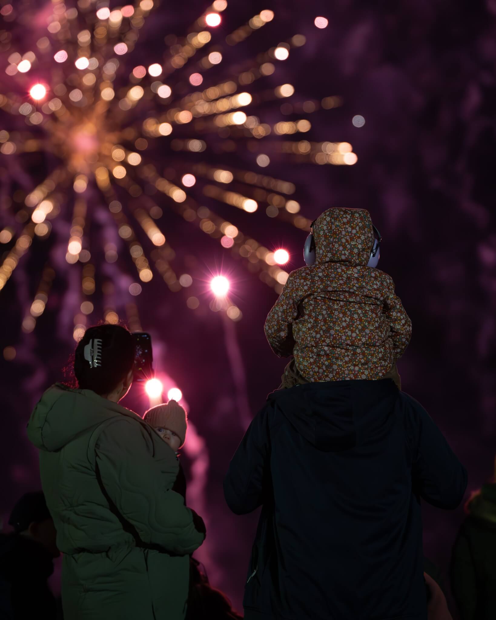 Family with a child on shoulders watching fireworks