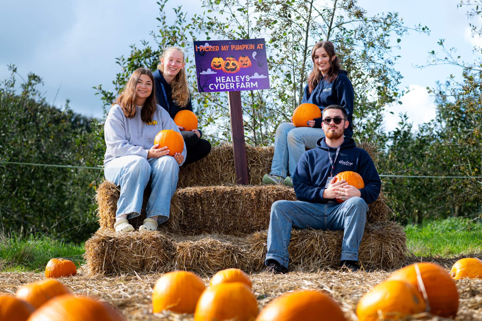 Healey's team with pumpkins beside the farm's Halloween sign