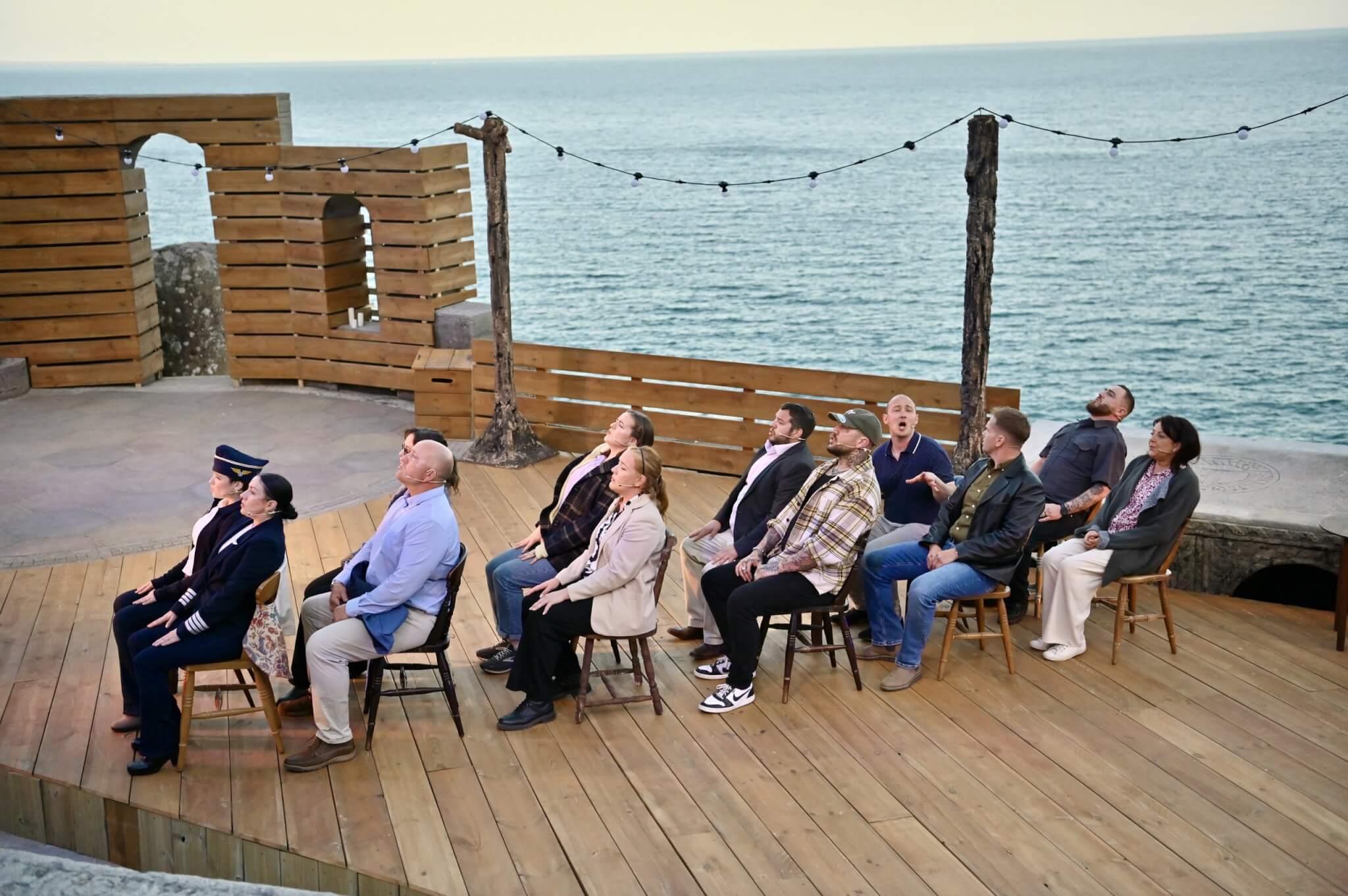 Come From Away cast seated on the Minack stage with the Atlantic behind