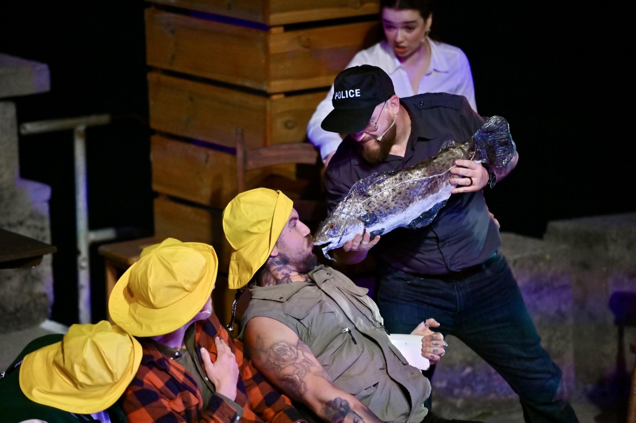 Come From Away cast in yellow sou'westers with a large fish on the Minack stage