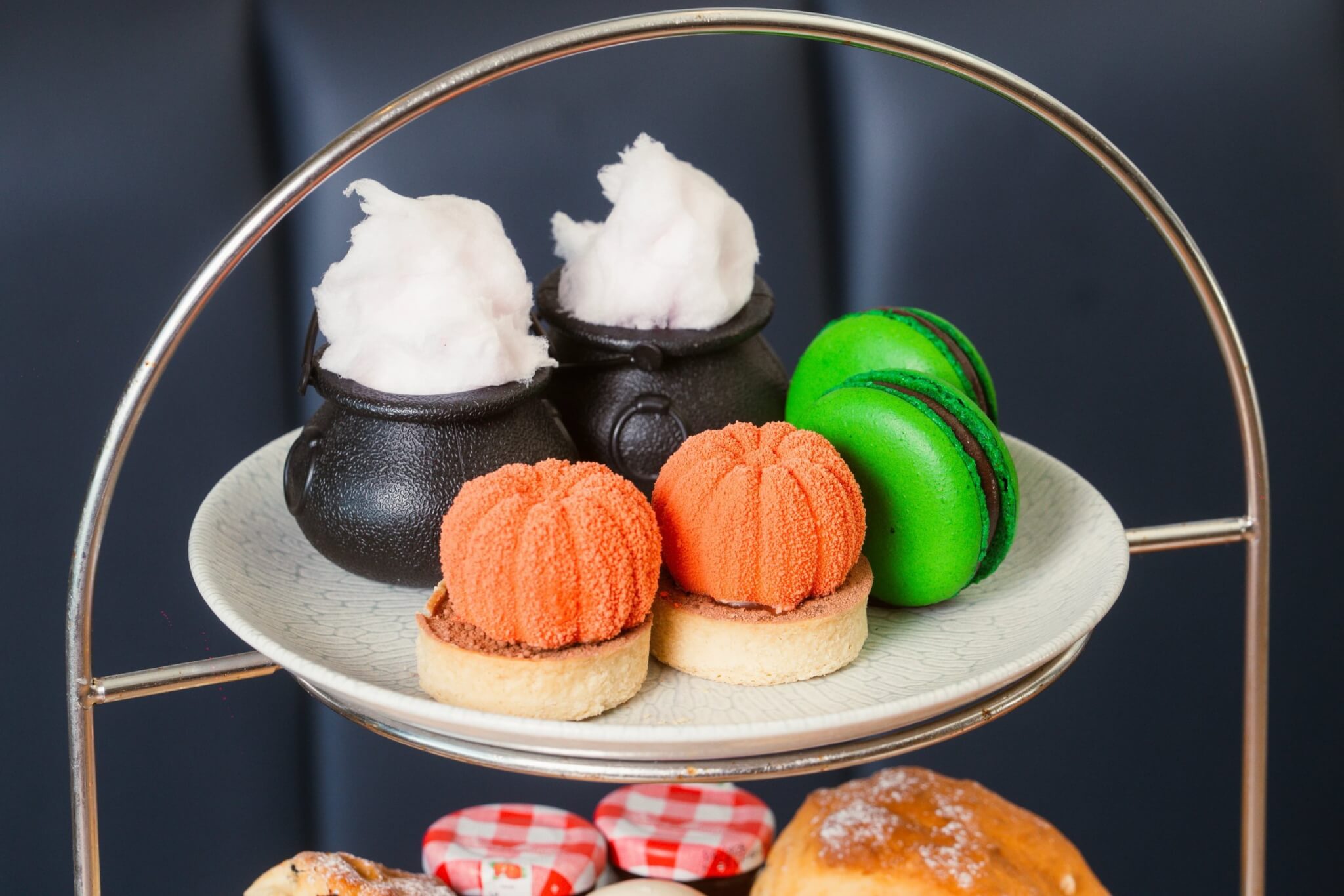 Lime jelly cauldrons, pumpkin cheesecakes and green macarons on an afternoon tea stand