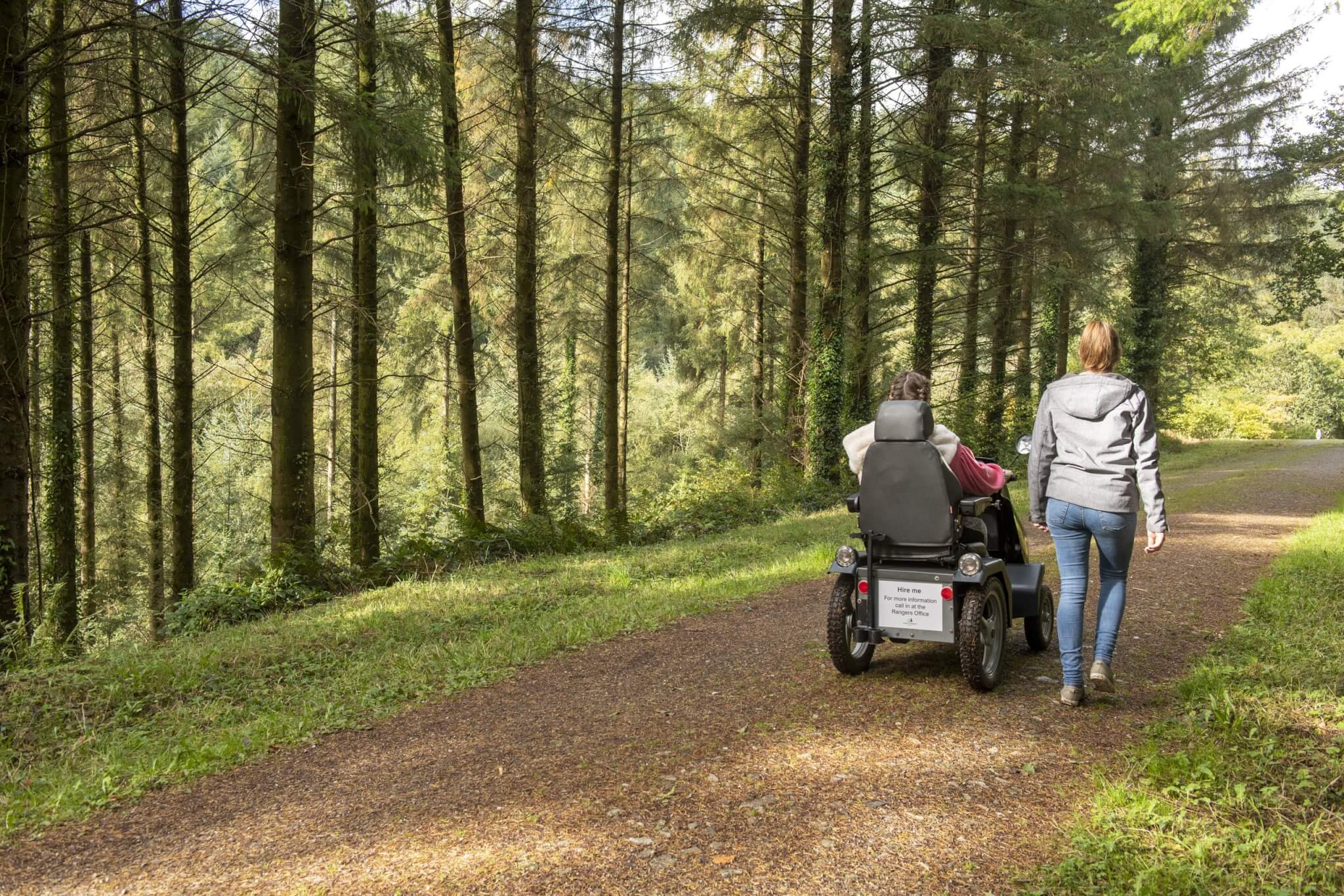 A walker beside an all-terrain mobility scooter on a forest track