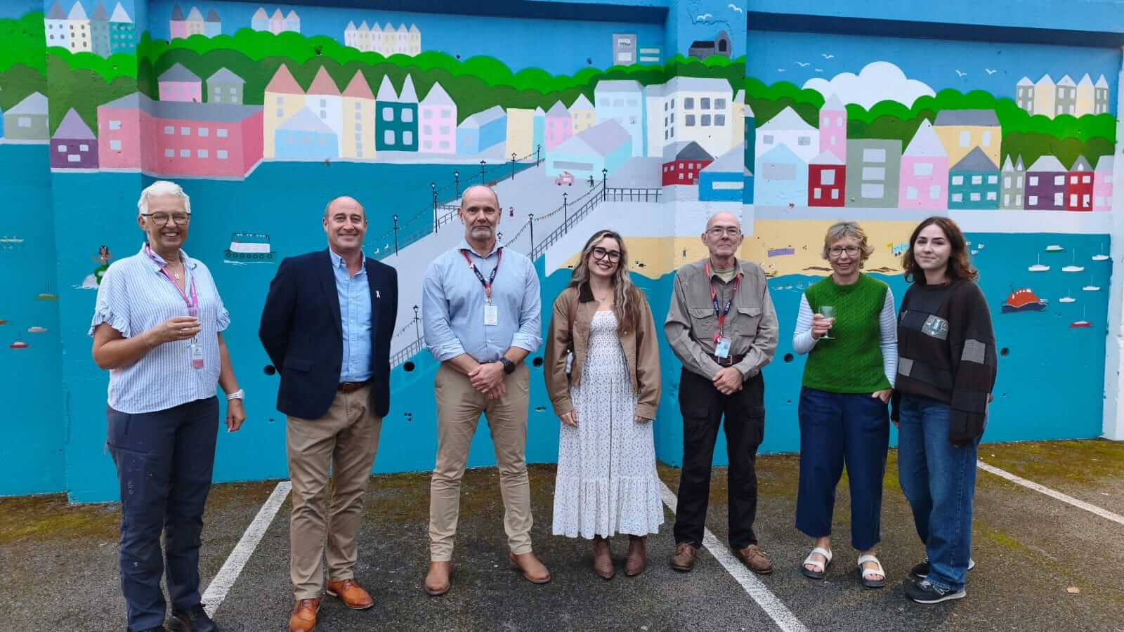 Seven people standing in front of the Falmouth mural at Falmouth Marine School