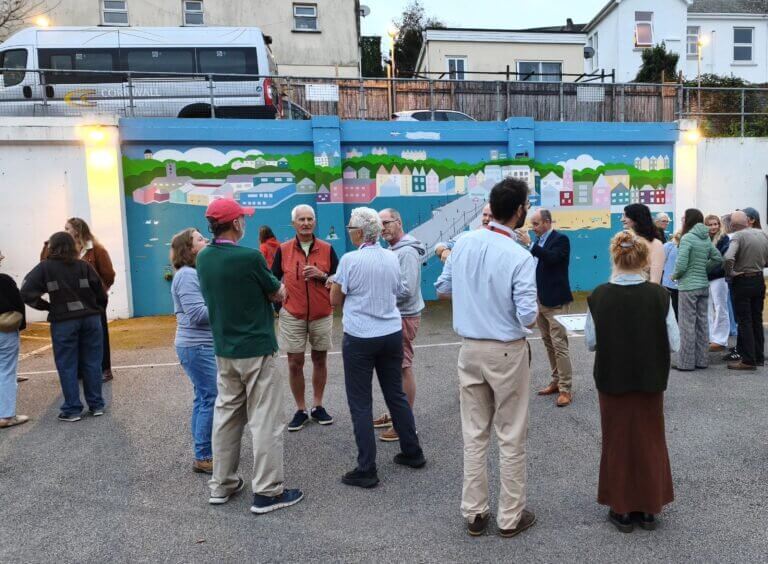 People gathered at dusk in front of the Falmouth mural