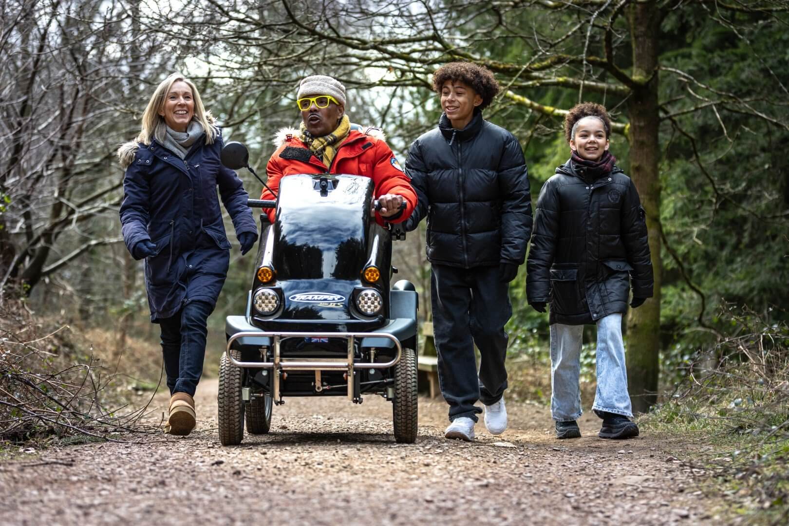 A family walking in the forest with an all-terrain mobility scooter