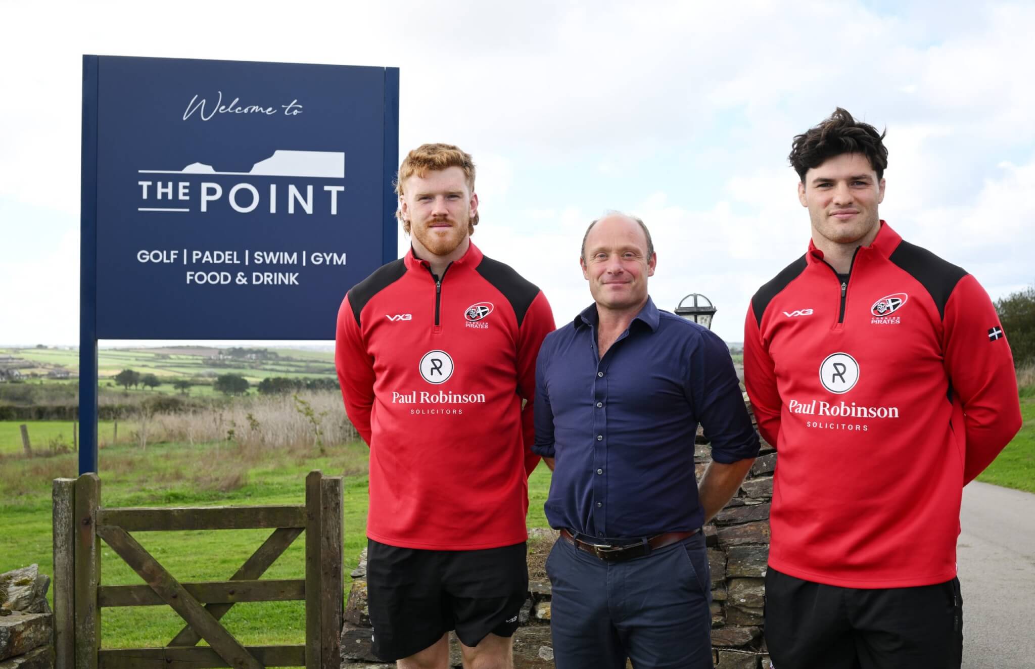 Tom O'Donnell of The Point with two Cornish Pirates players beside the resort's welcome sign at Polzeath
