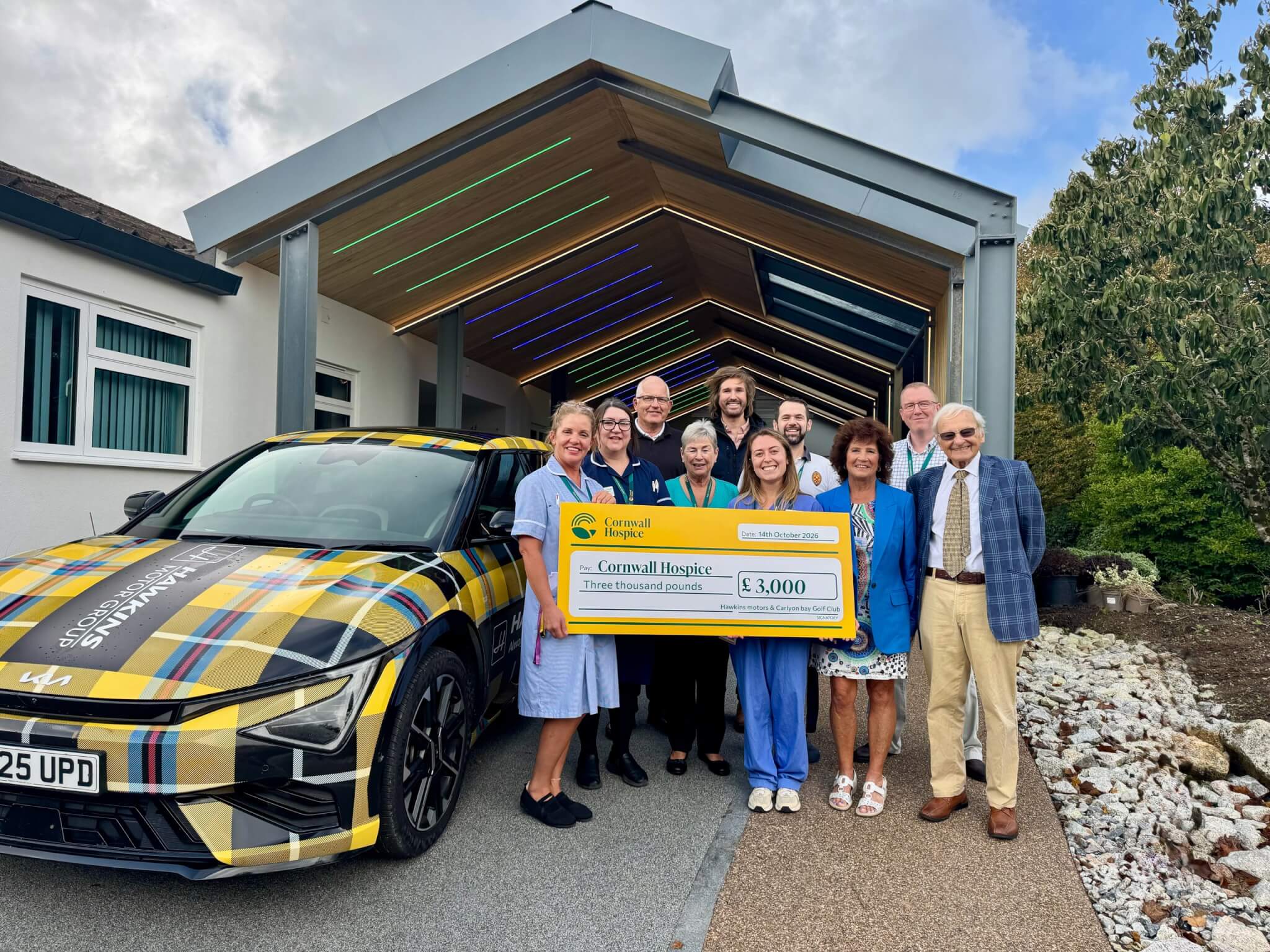 Cheque for £3,000 presented to Cornwall Hospice beside the Hawkins Motor Group tartan Kia EV6