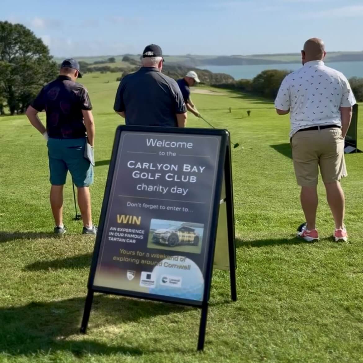 Charity day sign at the tee at Carlyon Bay Golf Club with golfers and the sea beyond