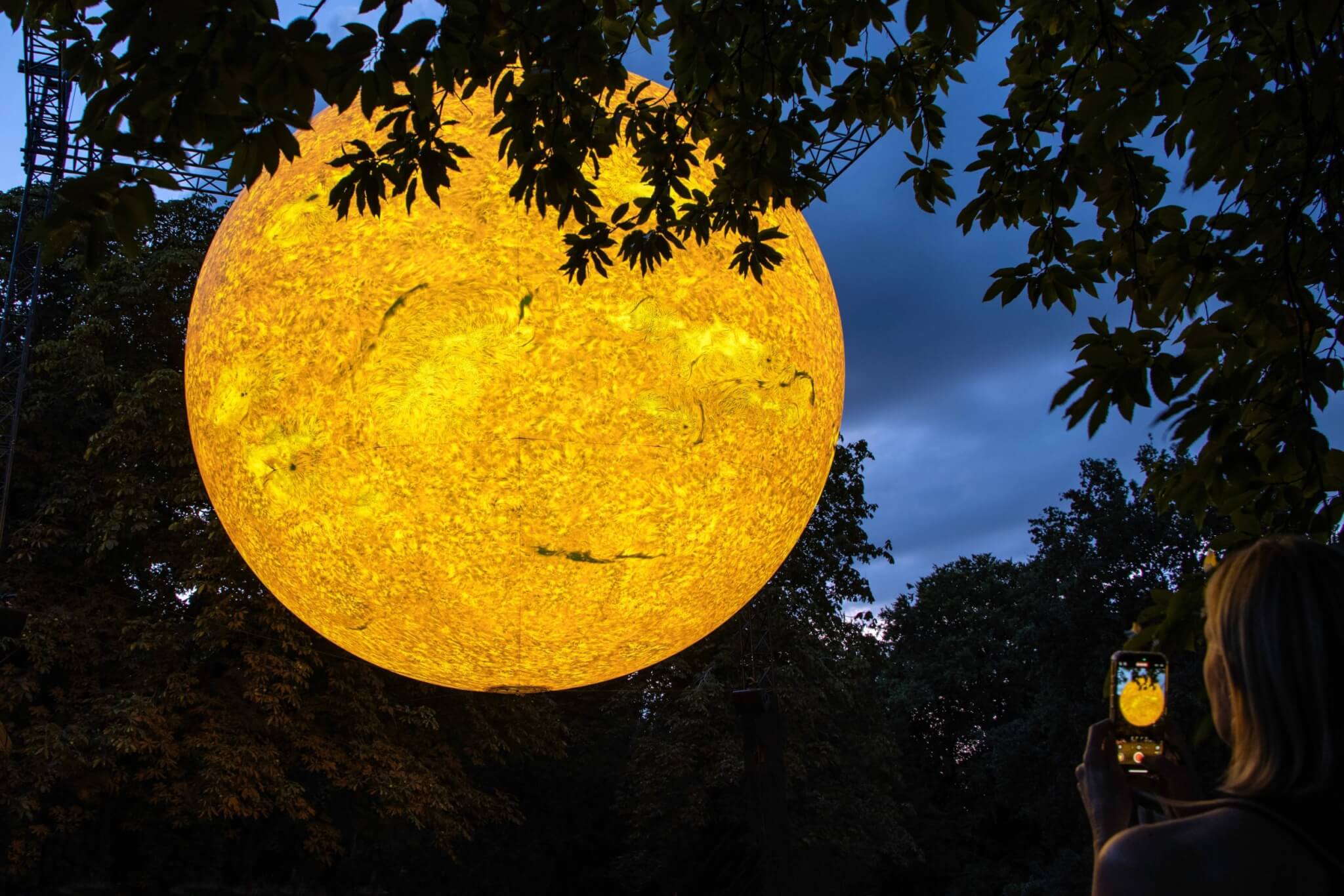 Helios Sun artwork glowing among trees at Basildon Park as a visitor photographs it