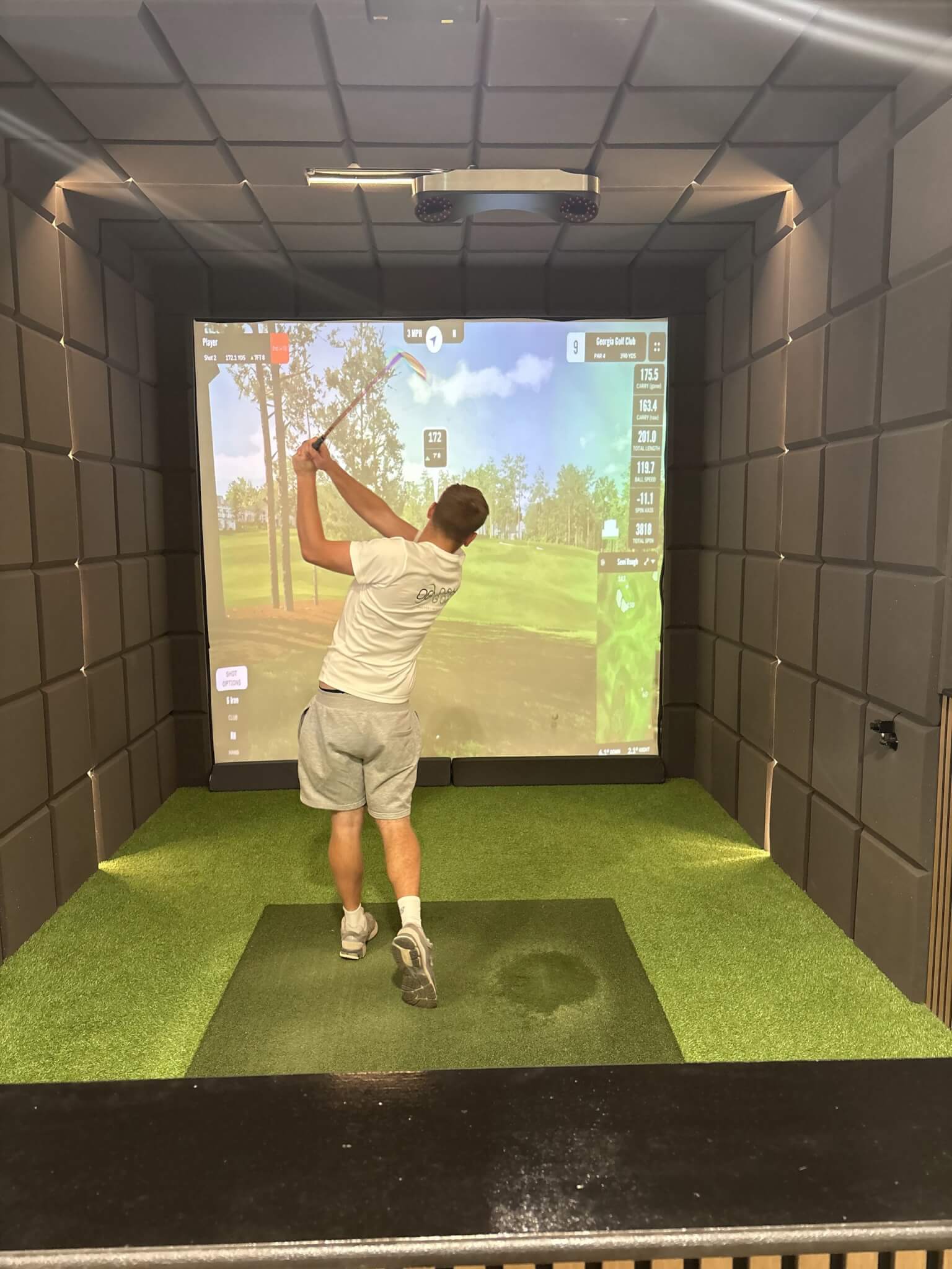 Henry O'Shaughnessy swinging a club in a golf simulator bay at OSH Golf