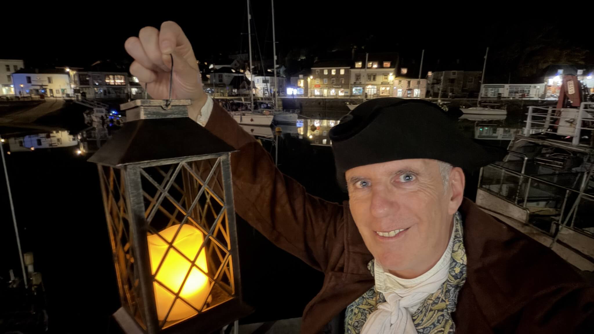 Ghost Walk Padstow guide in 18th-century costume holding a lantern by Padstow Harbour at night