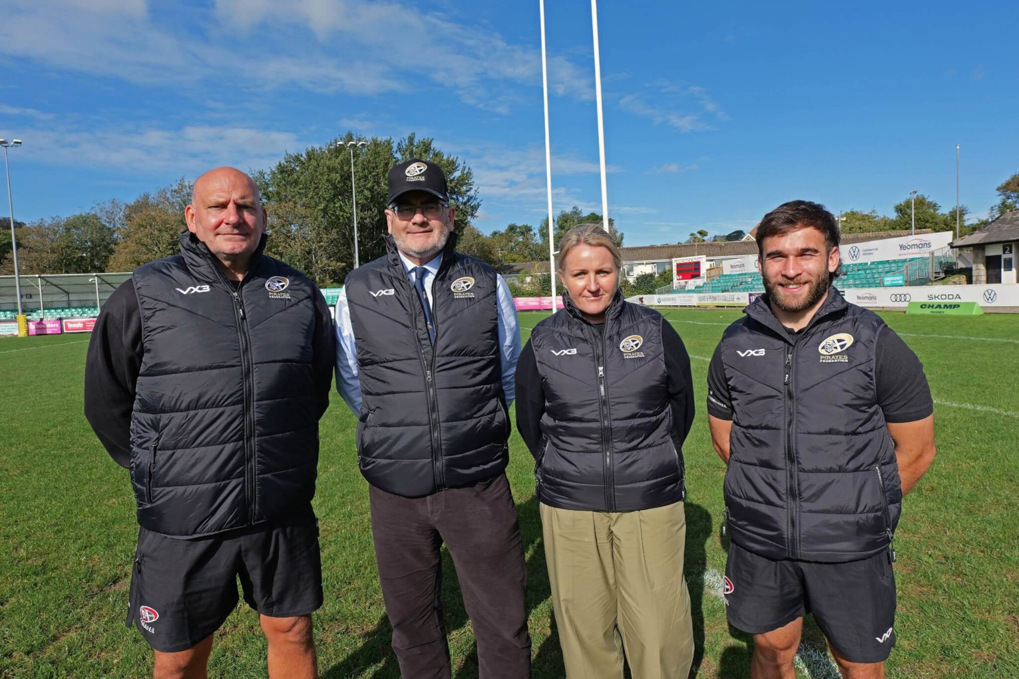 Four people in Pirates Foundation gilets standing on a rugby pitch in front of the posts