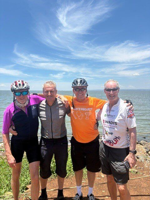 Four cyclists in kit standing by the water in Kenya