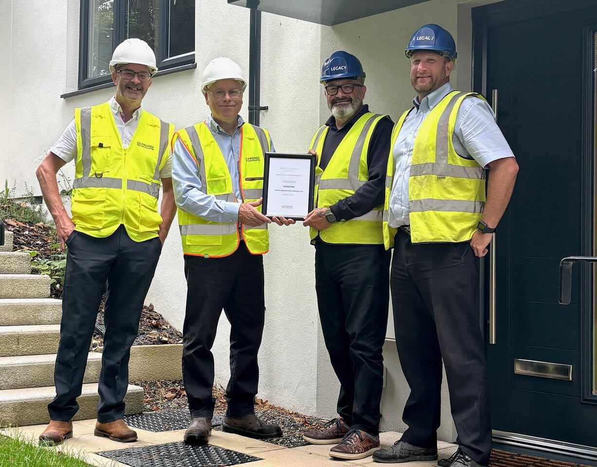 Four men in hi-vis and hard hats holding a framed award certificate outside a new home