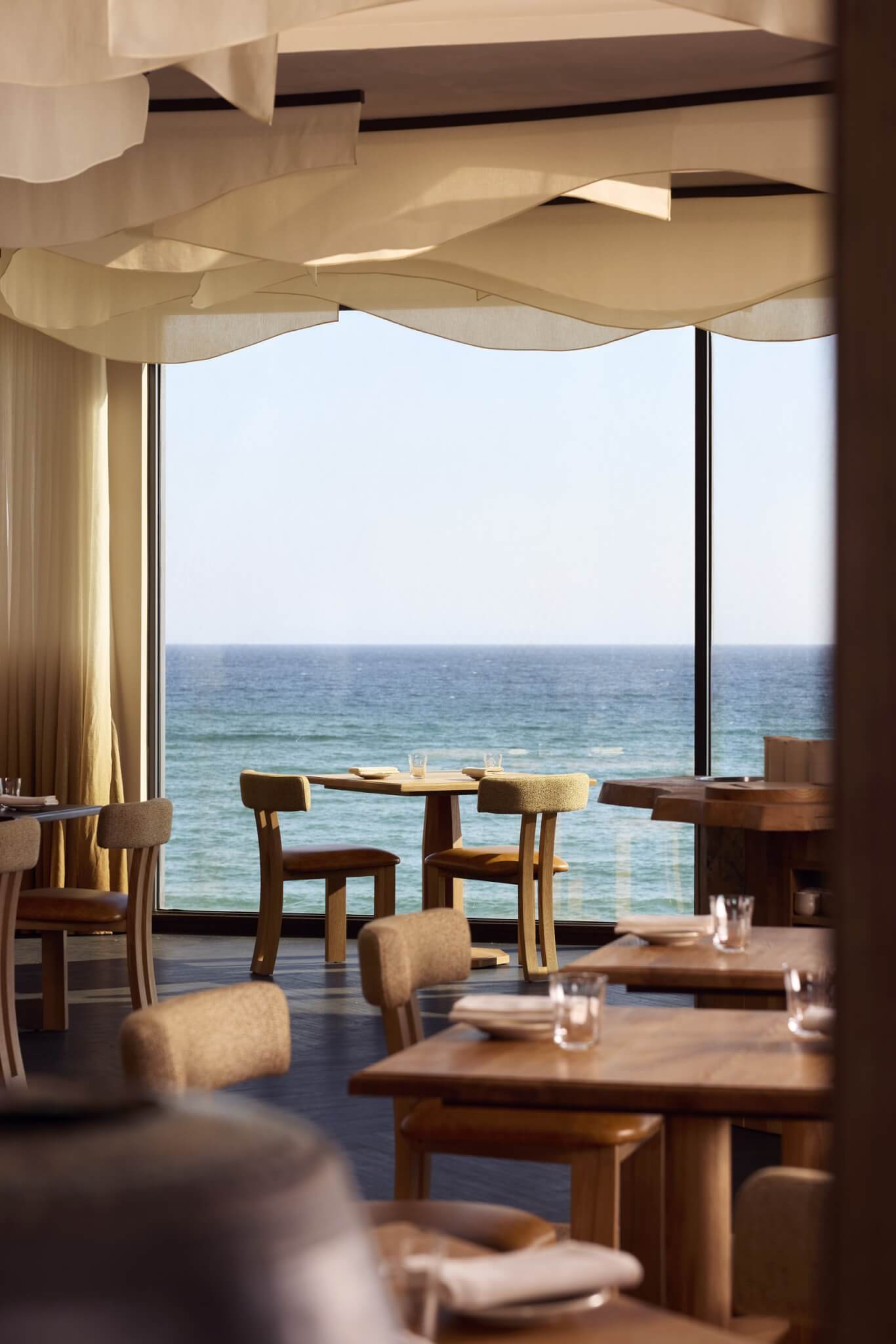 MOR dining tables beside floor-to-ceiling windows overlooking the sea