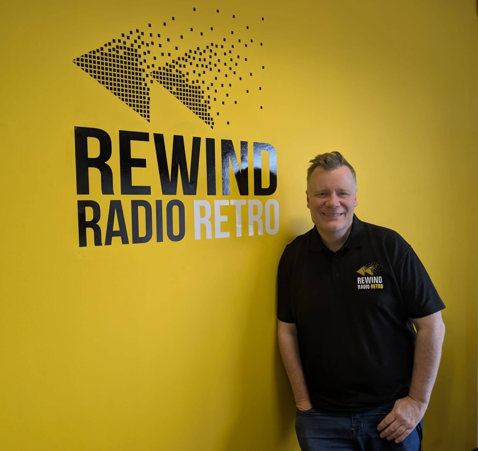 Matt Shepherd beside the Rewind Radio Retro logo on a yellow wall