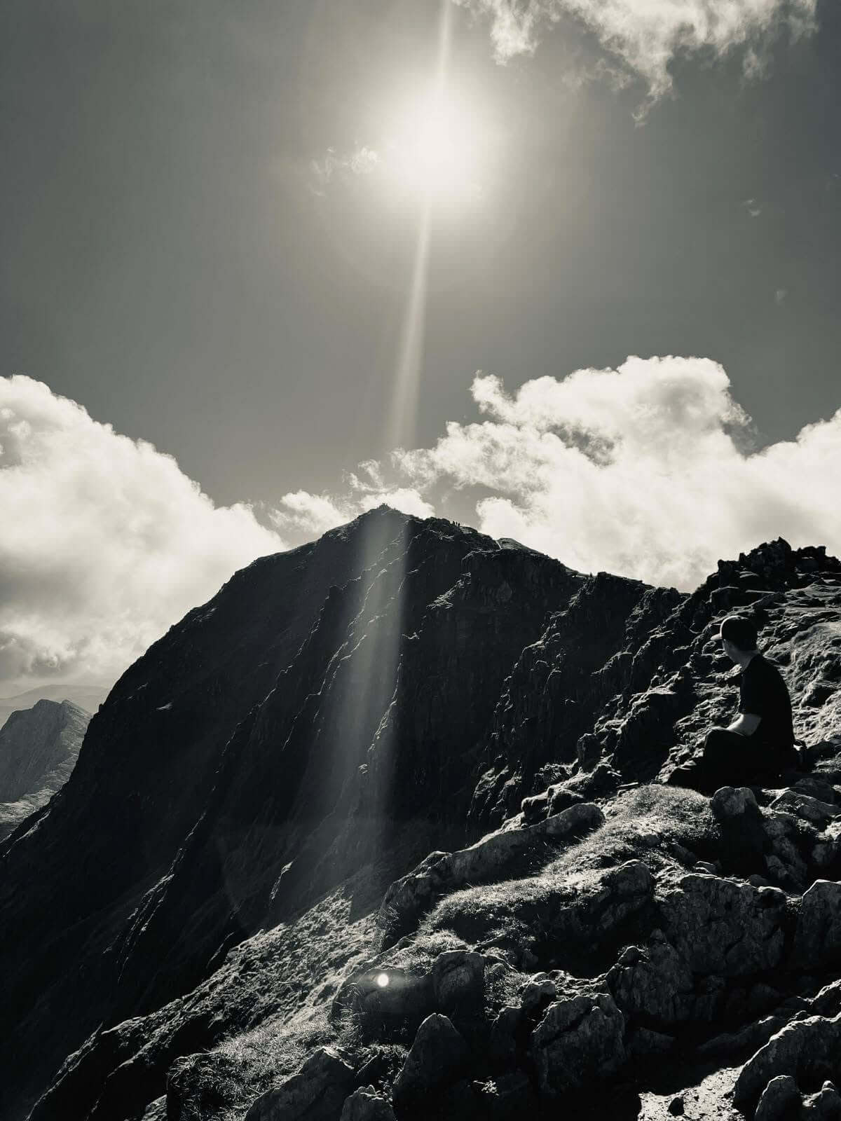 Walker sitting on rocks looking towards a mountain peak in sunlight