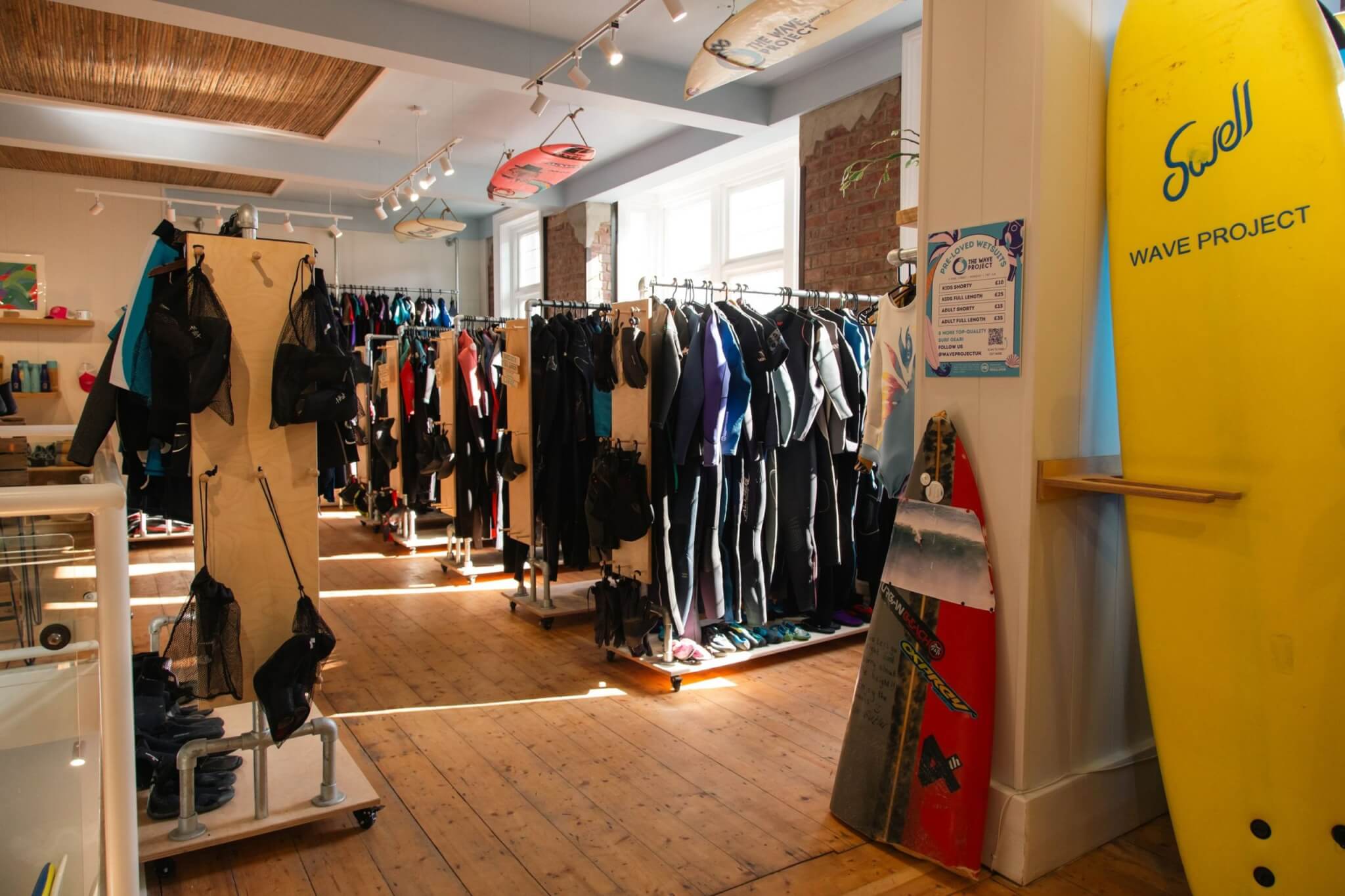 Rails of pre-loved wetsuits and surfboards inside The Wave Project shop