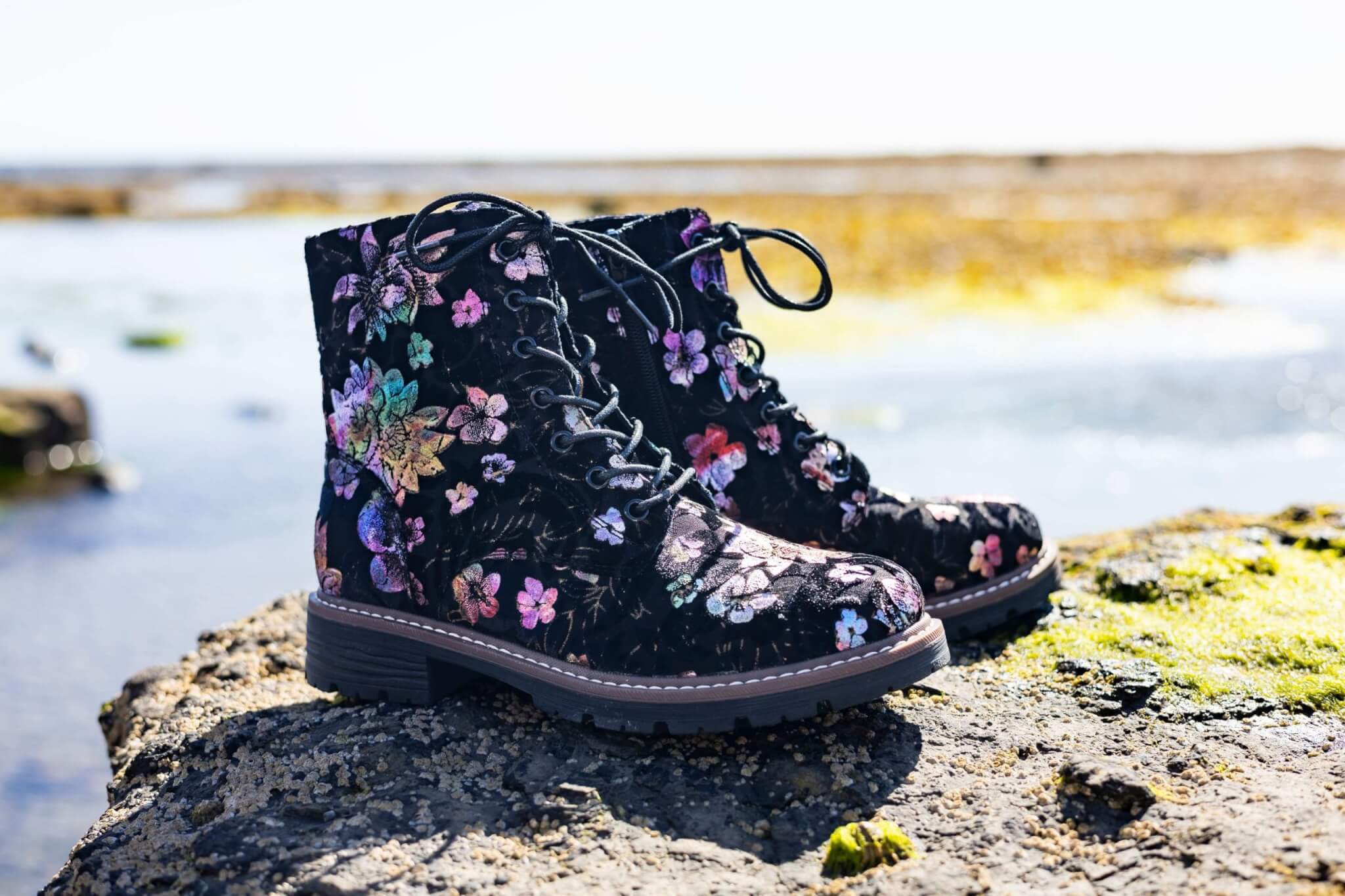 Black floral lace-up Pavers boots on a rock beside the sea