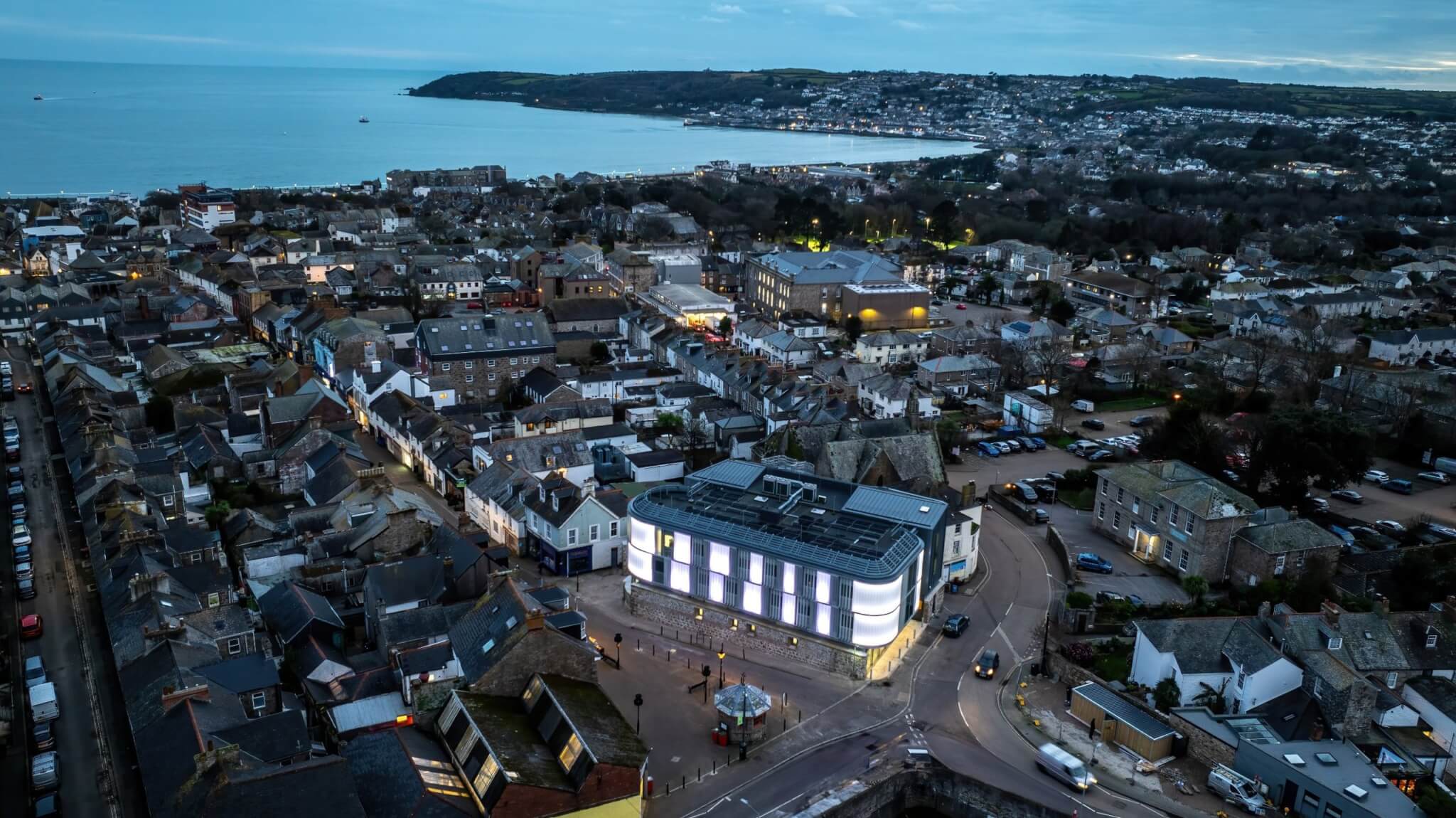 Aerial view of Penzance at dusk with the Pixel building lit up and Mount's Bay beyond