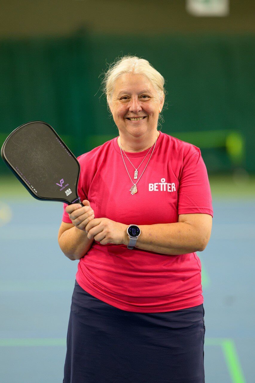 Pickleball player in a pink Better shirt smiling with her paddle