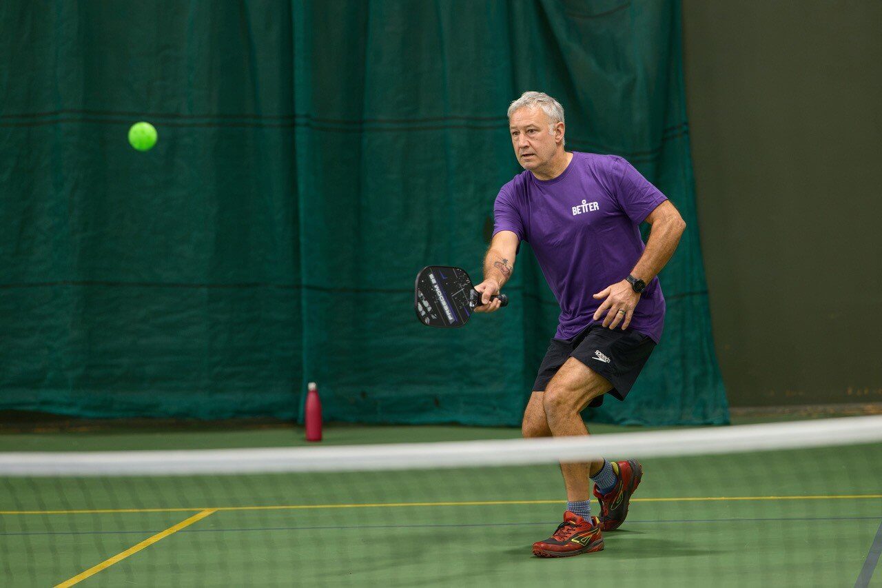Pickleball player in a purple Better shirt returning a shot